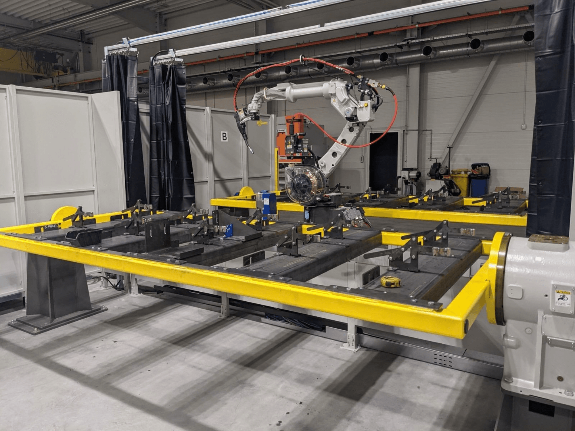 Vorderansicht des Roboterarms PANASONIC TAWERS TM-2000WG3, der über einem gelben Arbeitstisch mit Metallteilen für die Montage positioniert ist.
