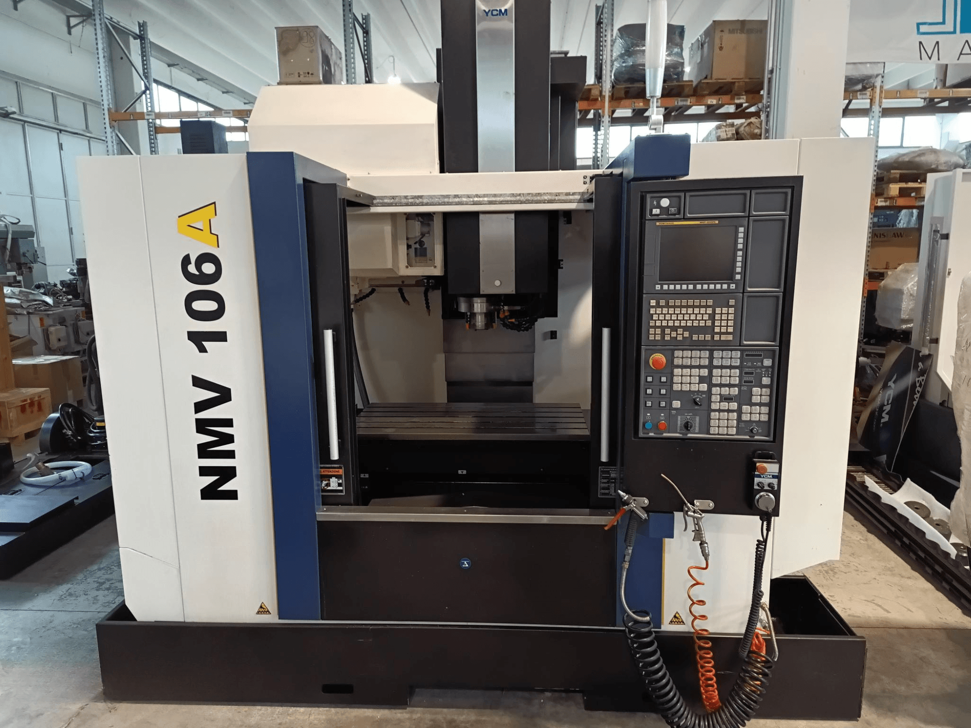 YCM NMV 106A Bearbeitungszentrum, Vorderansicht, mit Bedienfeld mit Tasten und Kühlmittelschläuchen.