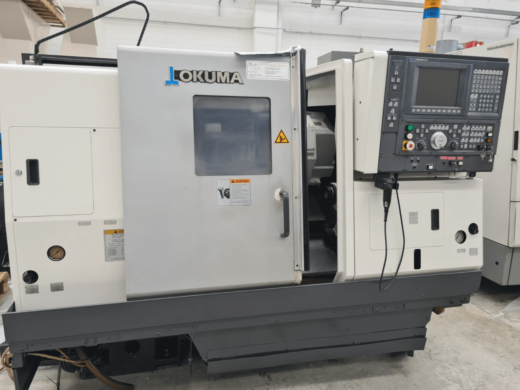 Okuma LB 300M X 500 Horizontal-Drehmaschine in der Seitenansicht, mit Bedienfeld, Spindelzugang und Sicherheitshinweisen.