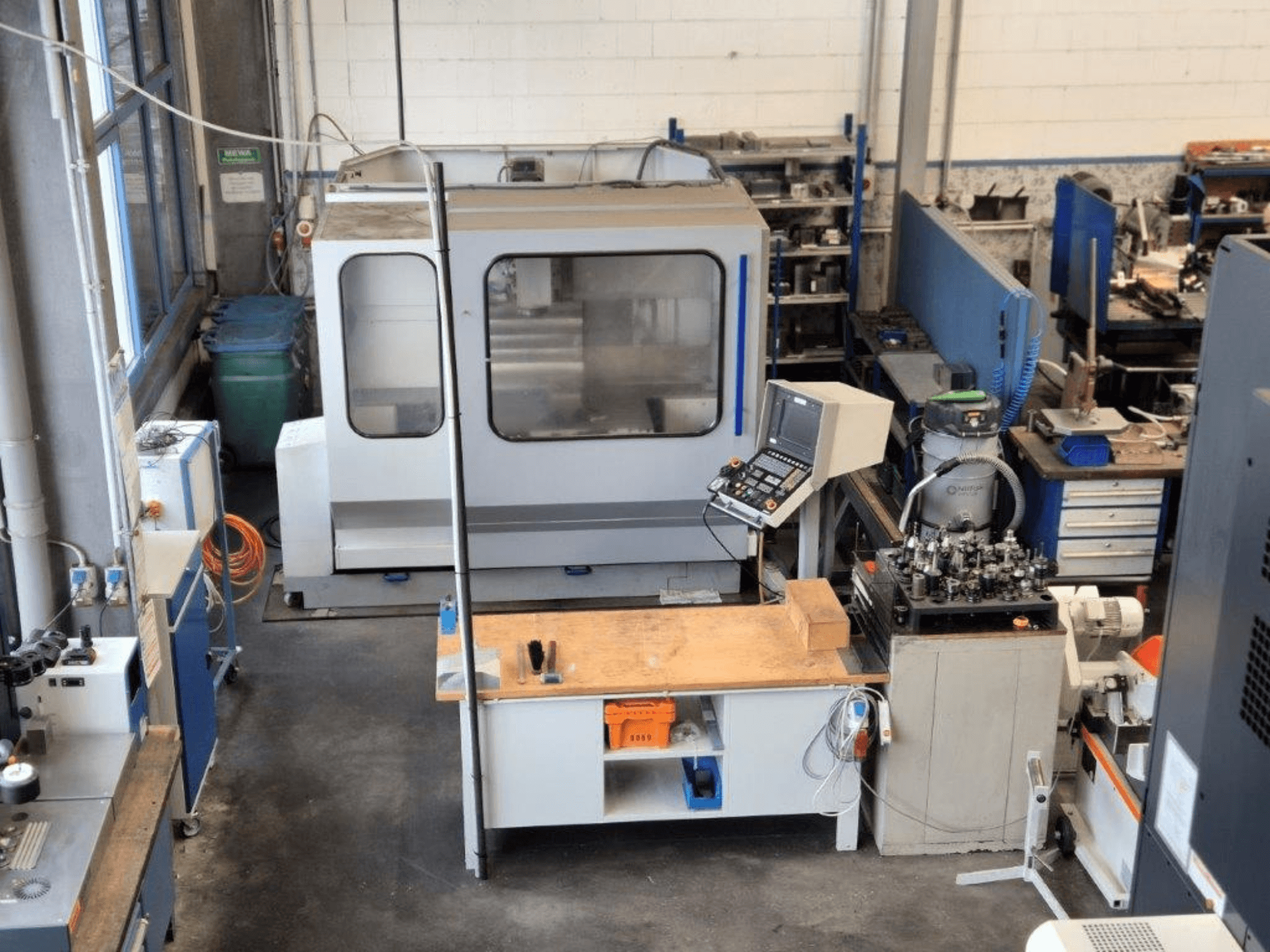 CNC-Fräsmaschine in einer Werkstatt, Vorderansicht, mit Bedienfeld, Arbeitsfläche und Werkzeugen im Hintergrund.