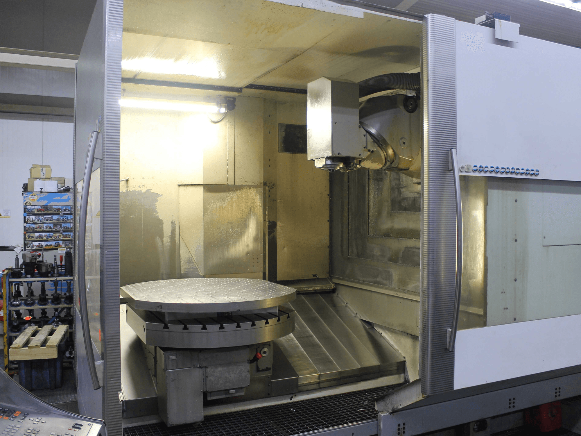 CNC-Fräsmaschine mit kreisförmigem Drehtisch und Schneidkopf, von vorne gesehen, mit metallischen Oberflächen und Beleuchtung.