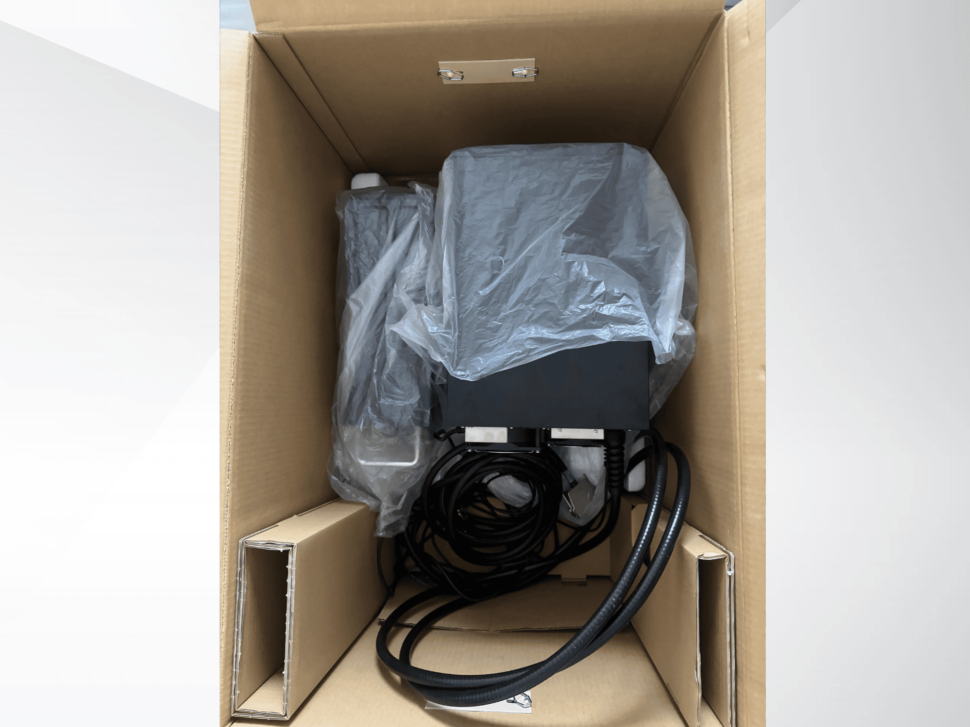 KEYENCE-Laserbeschriftungsgerät MD-X2500A in einem Karton, teilweise mit Plastikfolie abgedeckt, mit sichtbaren Kabeln und Bauteilen.