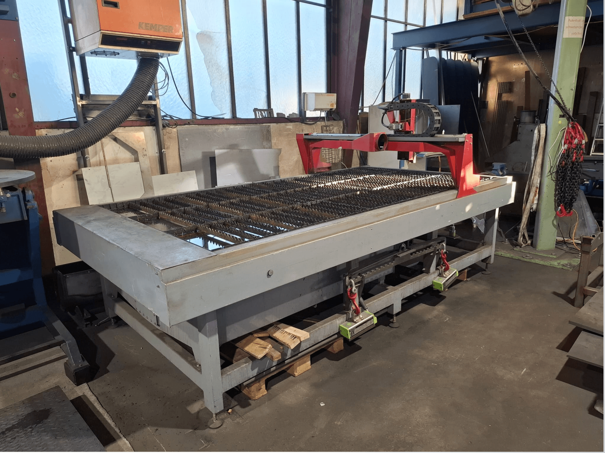 Die Plasmaschneidemaschine PLASMACUT 3015T in Seitenansicht, mit einem großen Schneidetisch mit Metalllamellen und rotem Rahmen.