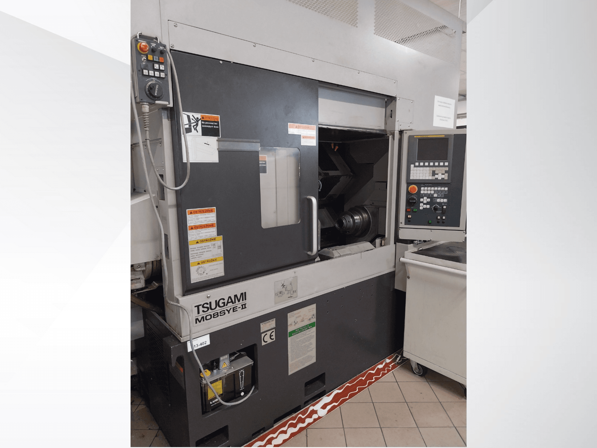 Tsugami M08SY-II CNC-Drehmaschine, Vorderansicht, zeigt Bedienfeld, Spindel und Ladebereich. Mit Sicherheitshinweisen und Markenetikett.