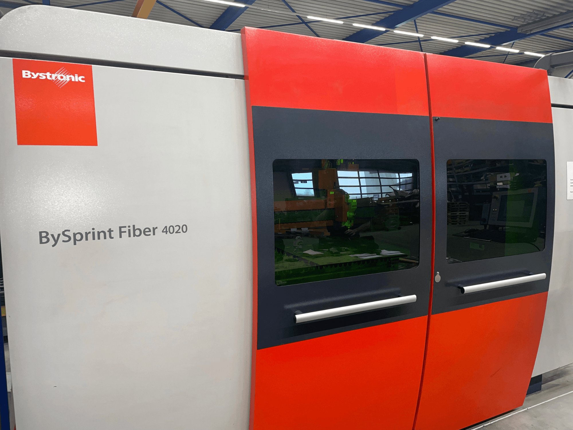 Bystronic BySprint Fiber 4020 in der Frontansicht, mit grauem und rotem Paneeldesign mit großen Fenstern und sichtbarer Steuerschnittstelle im Inneren.