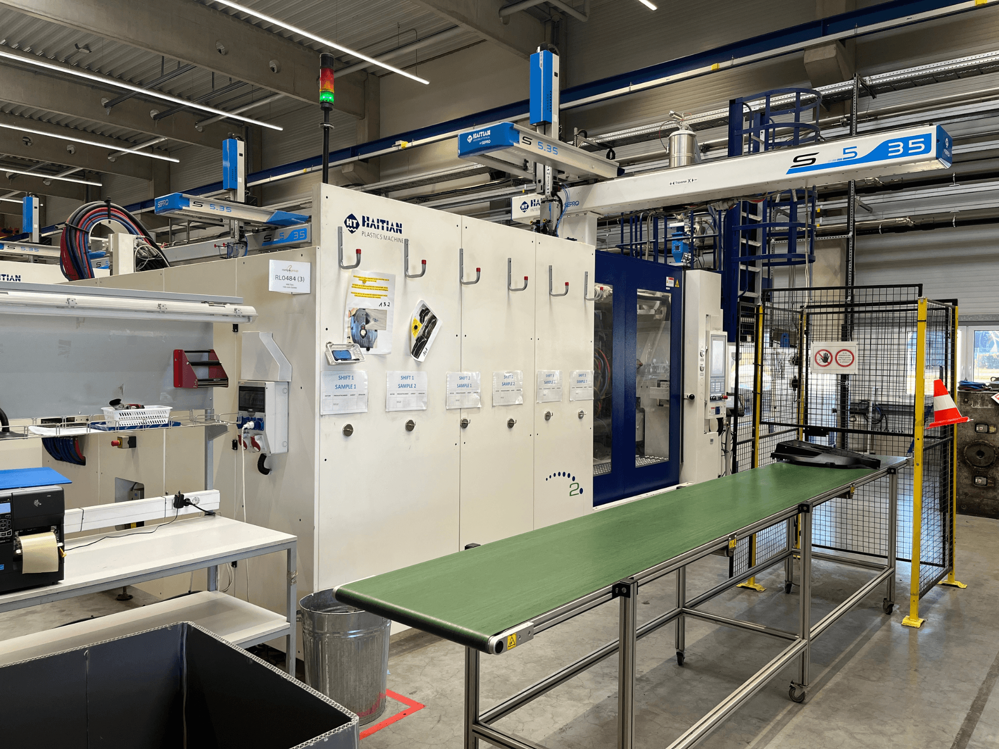 Haitianische Kunststoffmaschine S5-35 in einer Werkstatt; grüner Fördertisch, Sicherheitsschranken und Bedienfeld von vorne sichtbar.