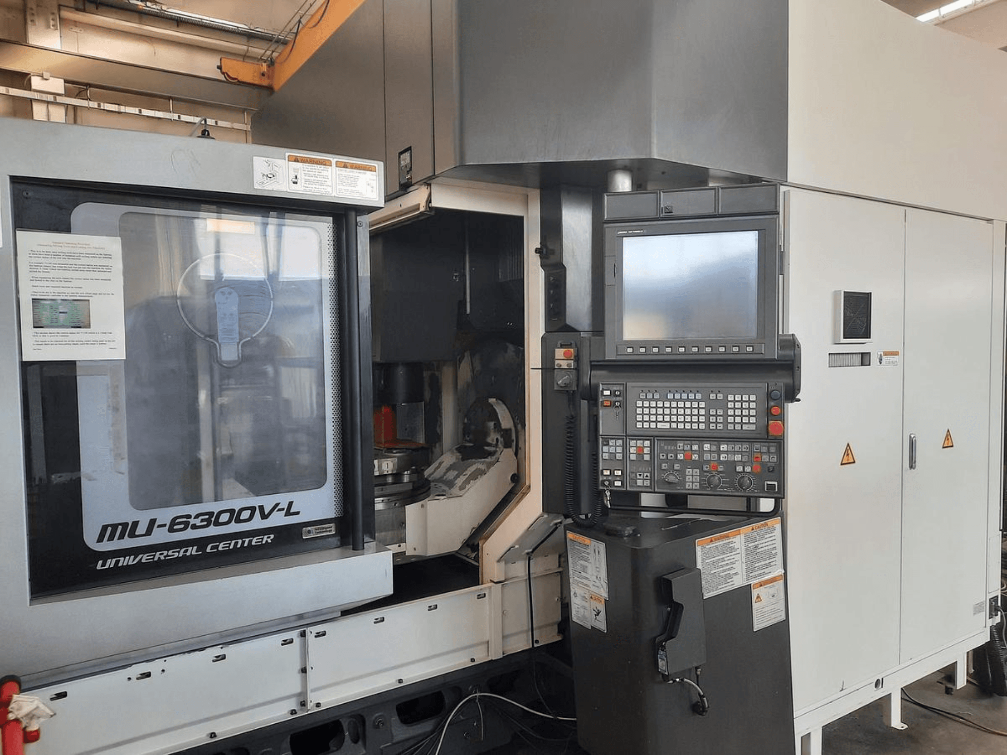 Die Maschine MU-6300V-L Universal Center in der Frontansicht mit sichtbarem Bedienfeld, Bildschirm und Betriebsanleitung.