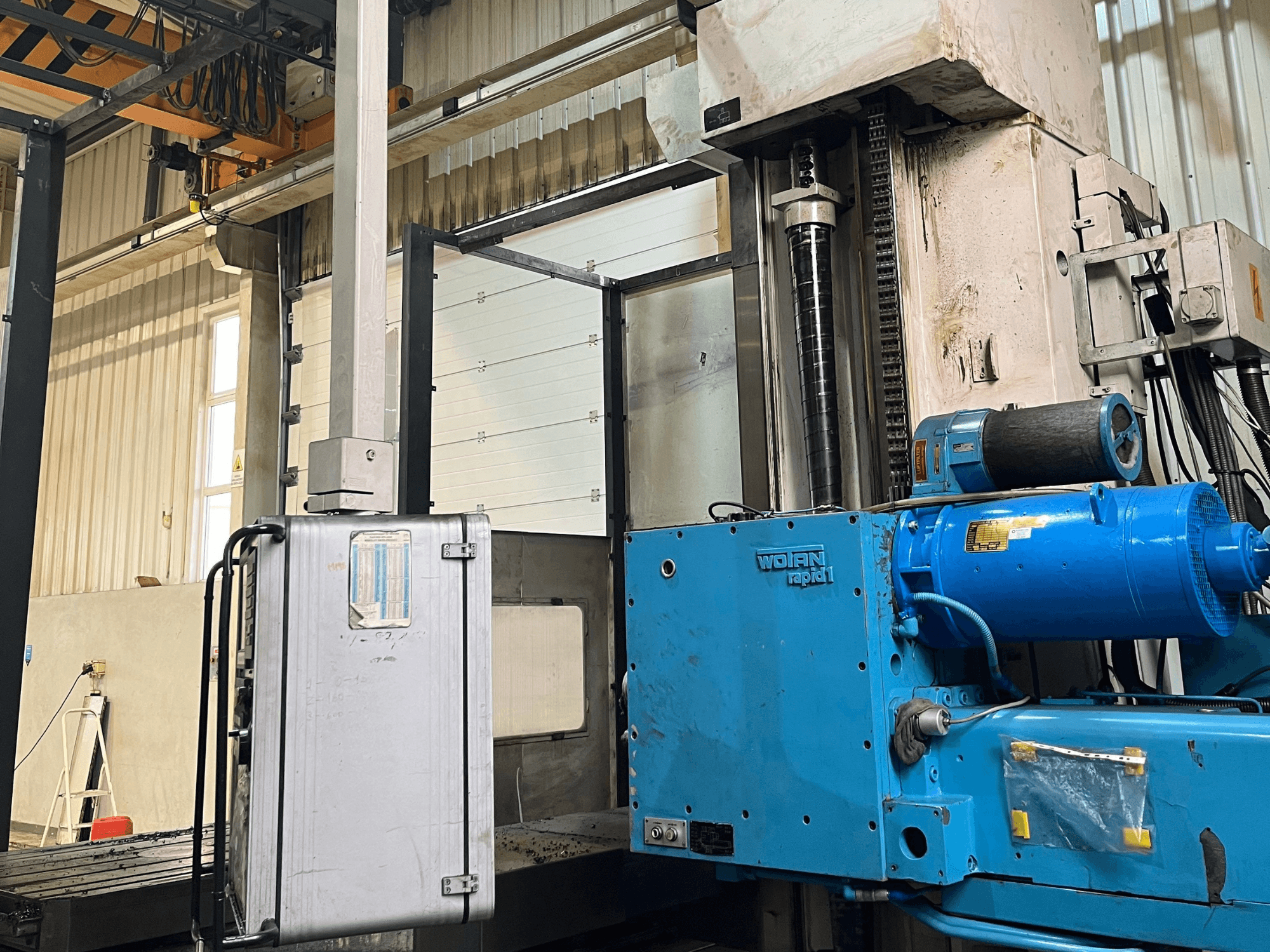 Bohrmaschine WOTAN Rapid 1 in Blau, Seitenansicht, mit Motor, Bedienelementen und vertikaler Säule in einer Werkstattumgebung.