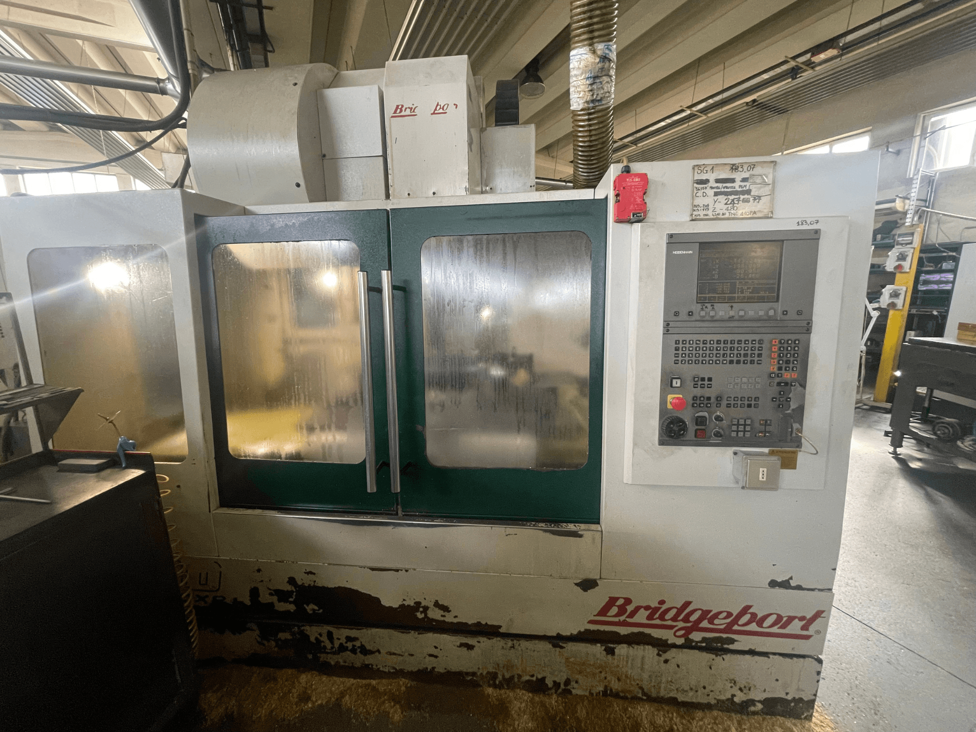 Vertikales Bearbeitungszentrum Bridgeport VMC 1000/30, Vorderansicht mit Bedienfeld, mit abgenutzter Außenverkleidung und grünen Türen.