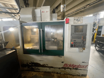 Vertikales Bearbeitungszentrum Bridgeport VMC 1000/30, Vorderansicht mit Bedienfeld, mit abgenutzter Außenverkleidung und grünen Türen.