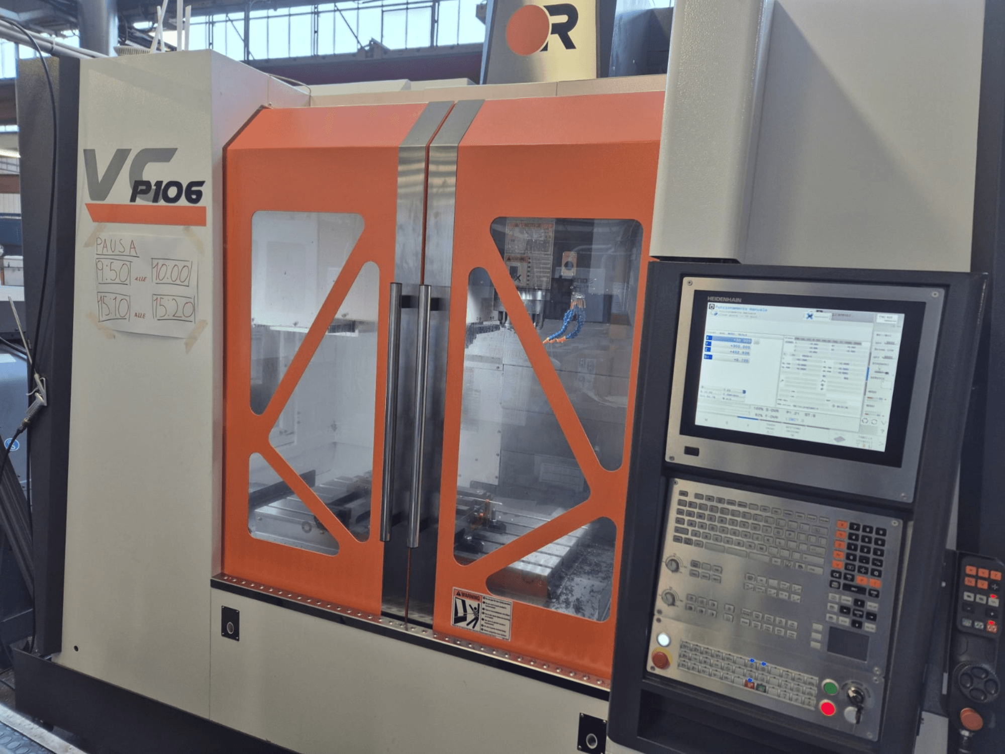 Alt-Text: Orangefarbene und graue CNC-Maschine VF P106, Vorderansicht, mit Anzeige eines Bedienfelds und geplanten Betriebszeiten auf Papier.