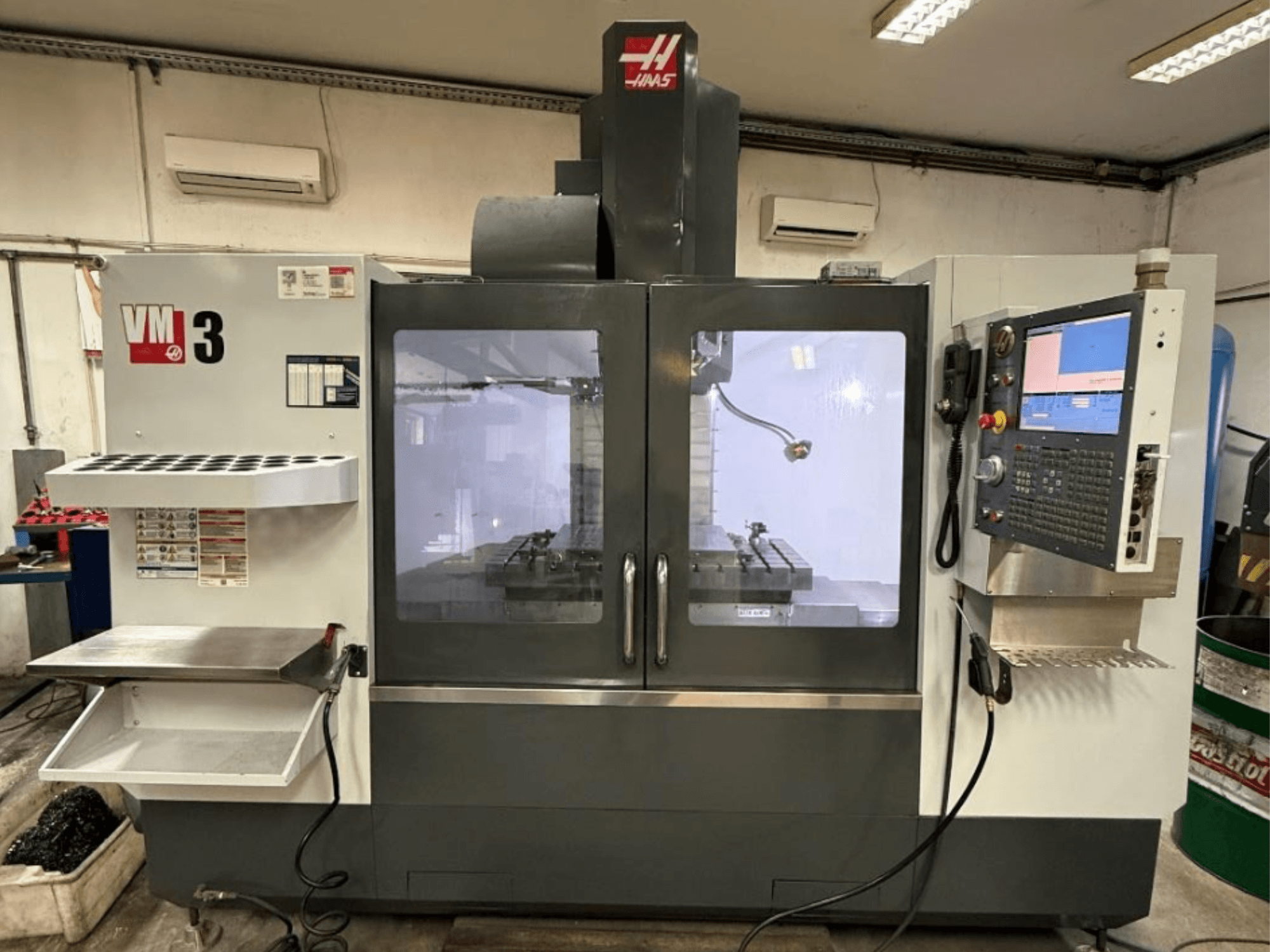 Vertikales Bearbeitungszentrum Haas VM-3 in der Vorderansicht, mit großem Bedienfeld und sichtbarem Arbeitsbereich mit Werkzeugen.
