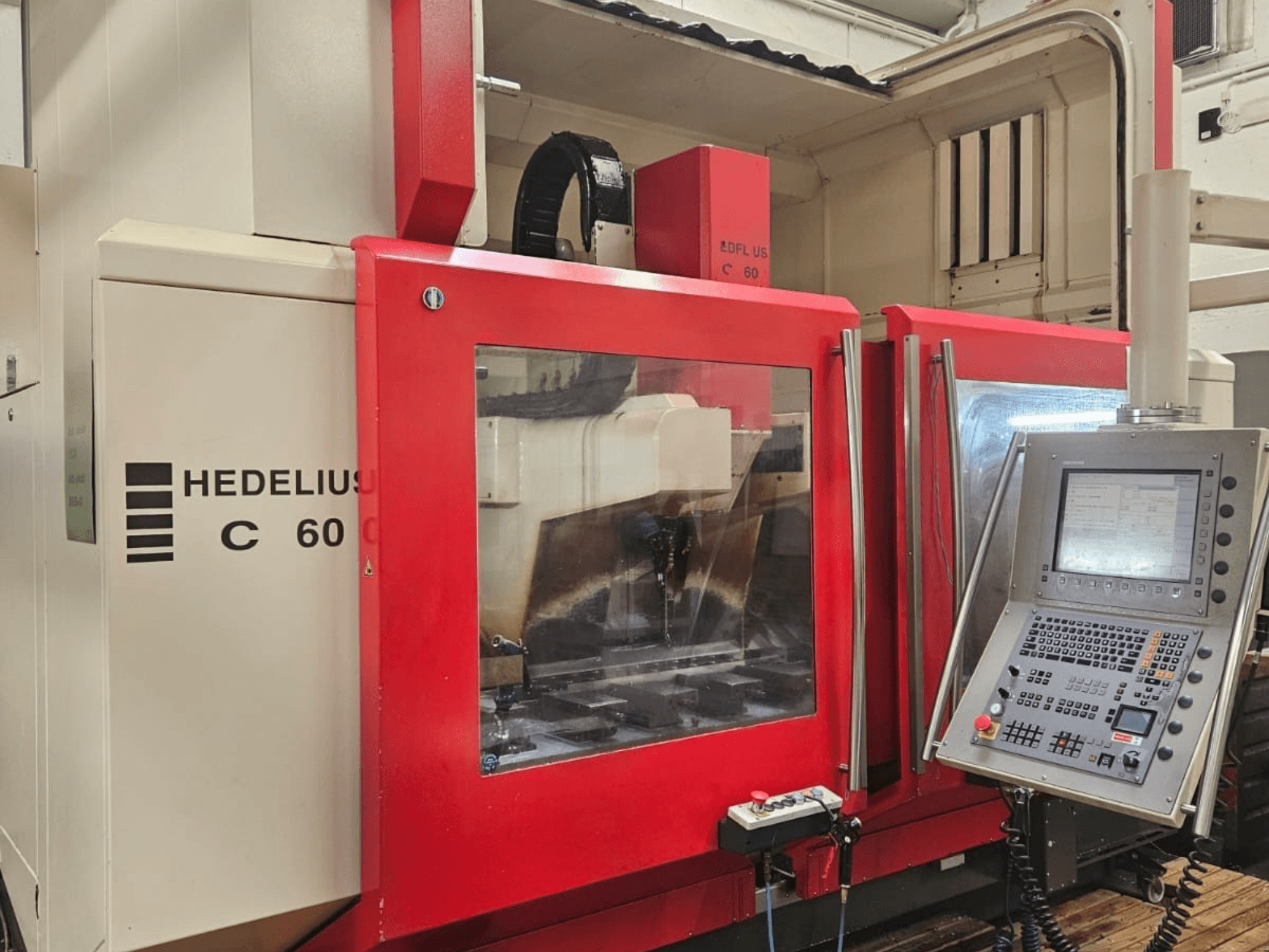Vertikales Bearbeitungszentrum HEDELIUS C60 von der Seite, mit roter Frontplatte und Bedienpult mit Display.