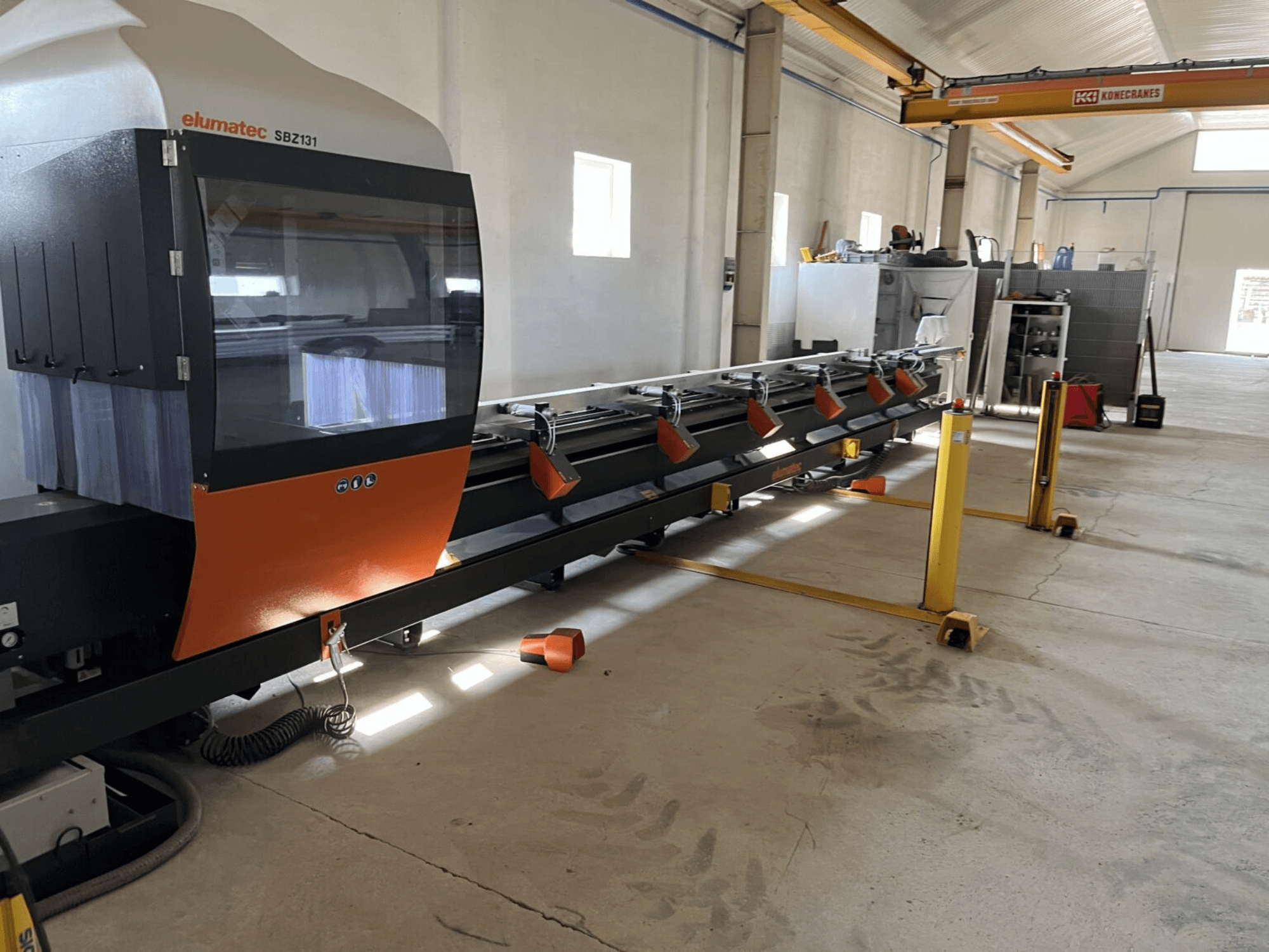 Elumatec SBZ131, Frontansicht einer Linear-Fräsmaschine in orange-schwarzem Design, in einer Werkstattumgebung.
