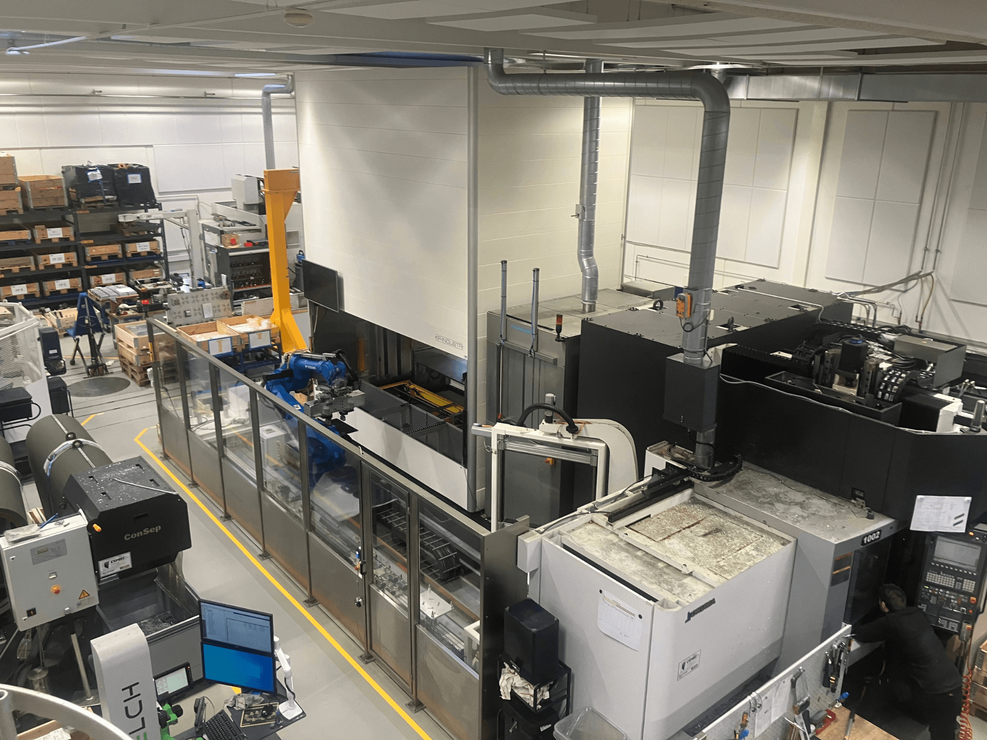 SSI SCHAFER Logimat-Automatisierungssystem in einem Lager, Vorderansicht; mit Roboterarm, Lagerregalen und Maschinen.