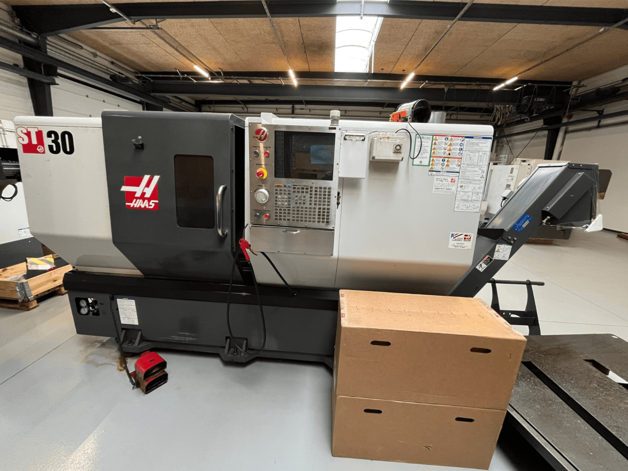 Haas ST-30 CNC-Drehmaschine, Vorderansicht, mit Bedienfeld mit Tasten, Not-Aus und zwei gestapelten Kartons.