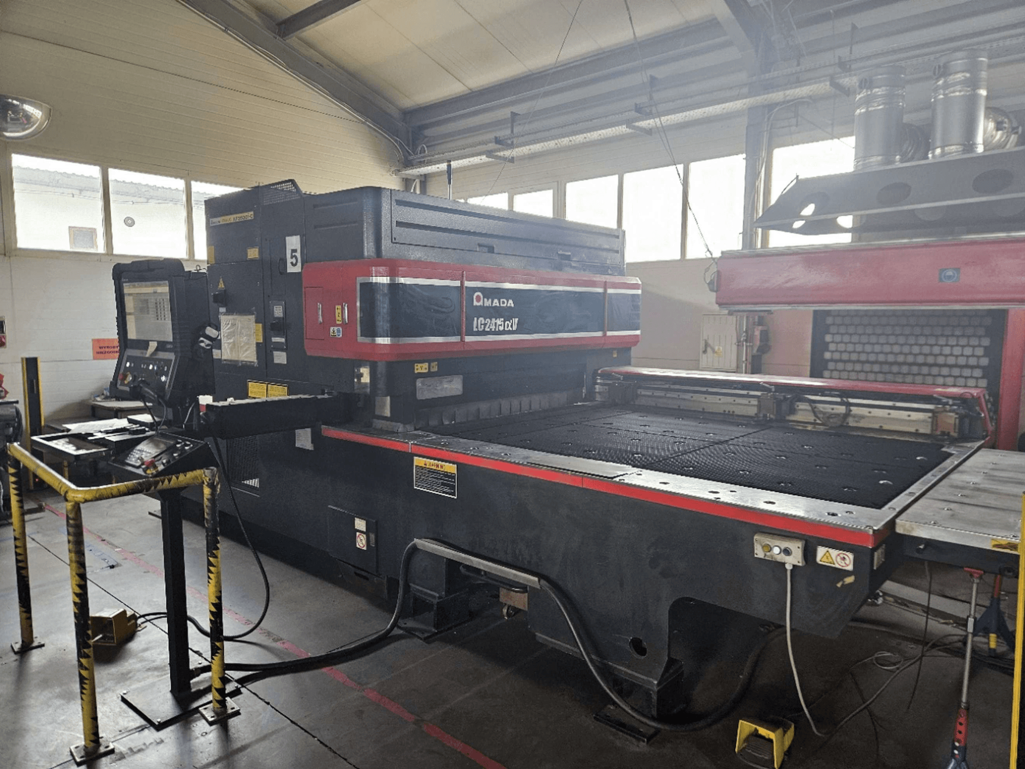 AMADA LC2415 Alpha 5 CO₂-Laserschneidmaschine, Vorderansicht mit Bedienfeld und Schneidetisch mit Sicherheitsbarrieren.