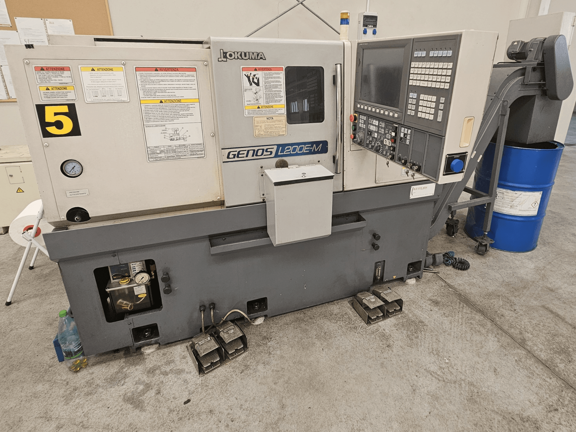 Okuma GENOS L200E-M Horizontal-Drehmaschine in der Vorderansicht, mit Bedienfeld, Etiketten und Kühlmittelrohr.