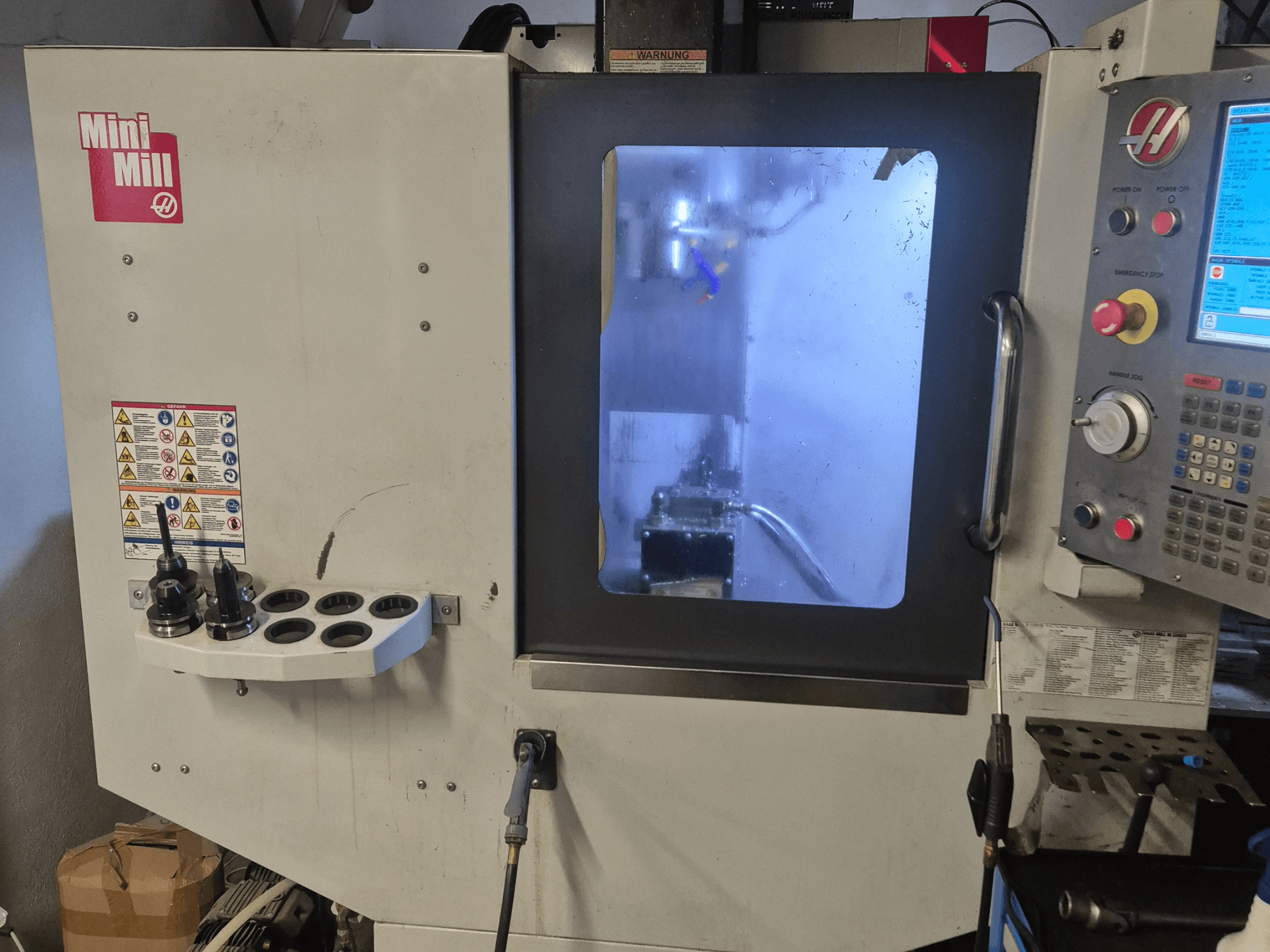 Frontansicht der HAAS Mini Mill mit Bedienfeld, Werkzeughaltern und Blick in den Bearbeitungsraum mit Kühlmittel.