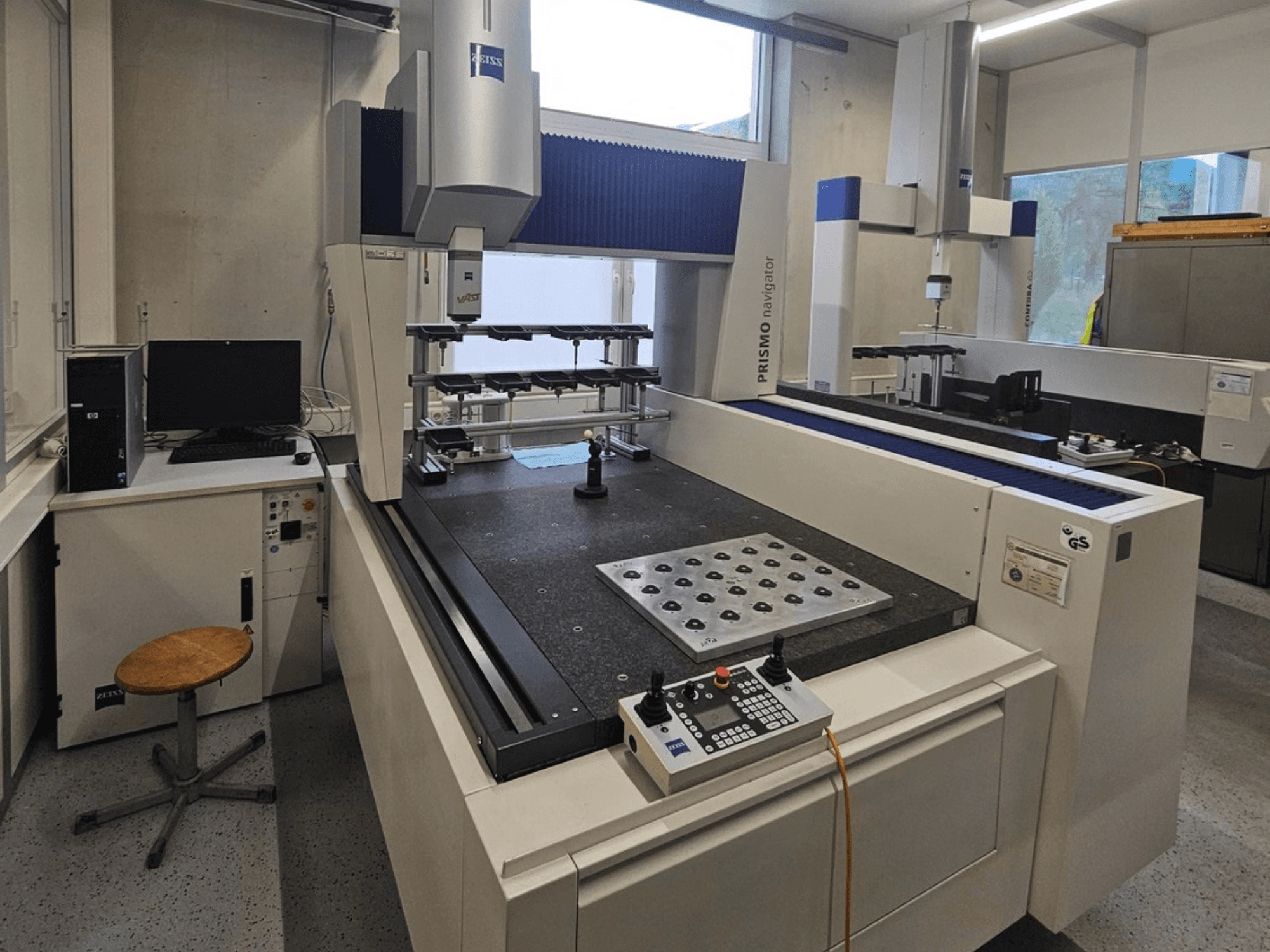 ZEISS Prismo Navigator 7 Koordinatenmessgerät in einem Labor, Vorderansicht mit Bedienfeld, Arbeitstisch und Monitor.