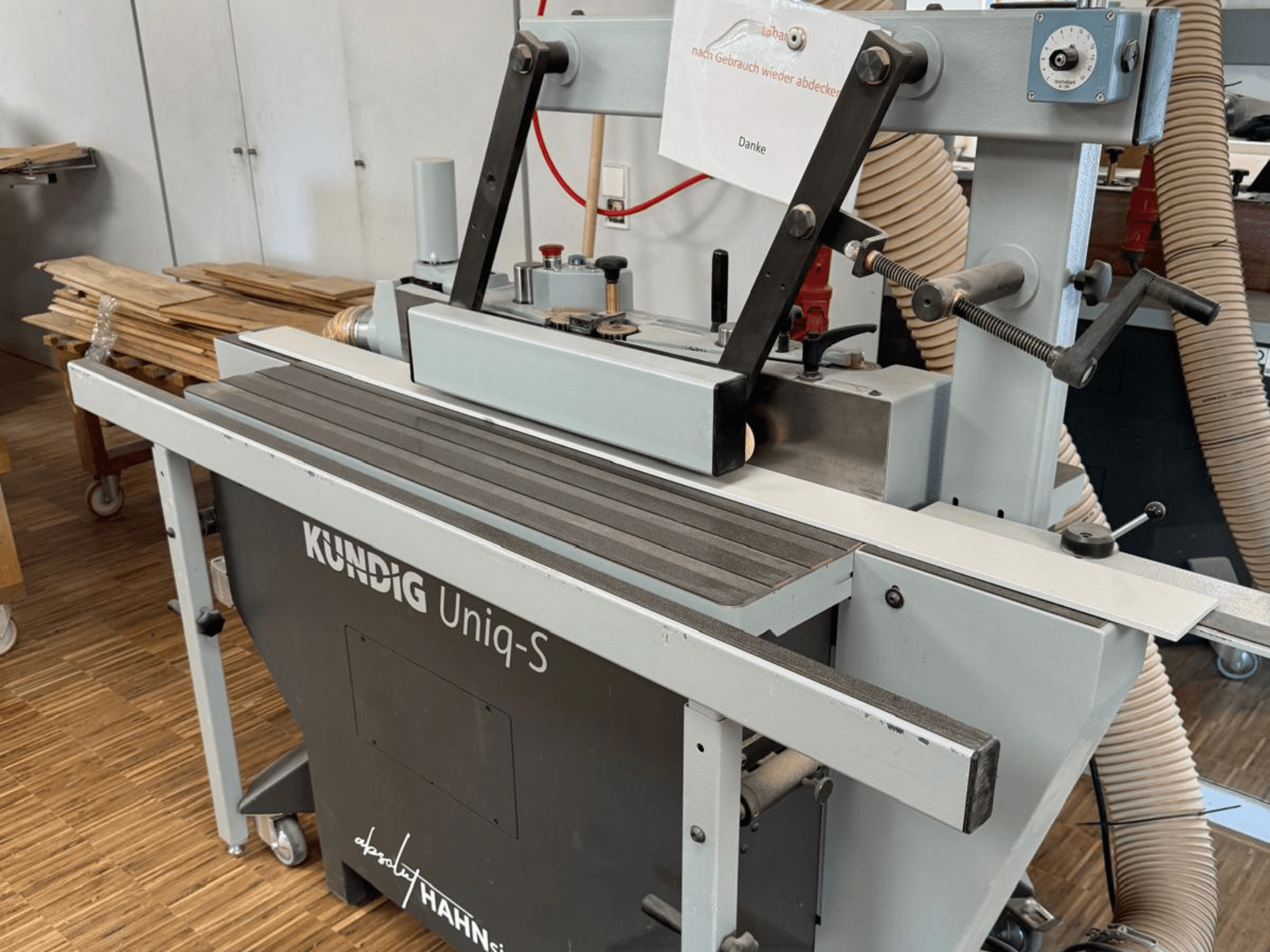 Kundig UNIQ-S Bandschleifmaschine in einer Werkstatt, Seitenansicht mit Schleifband und verstellbaren Tragarmen.