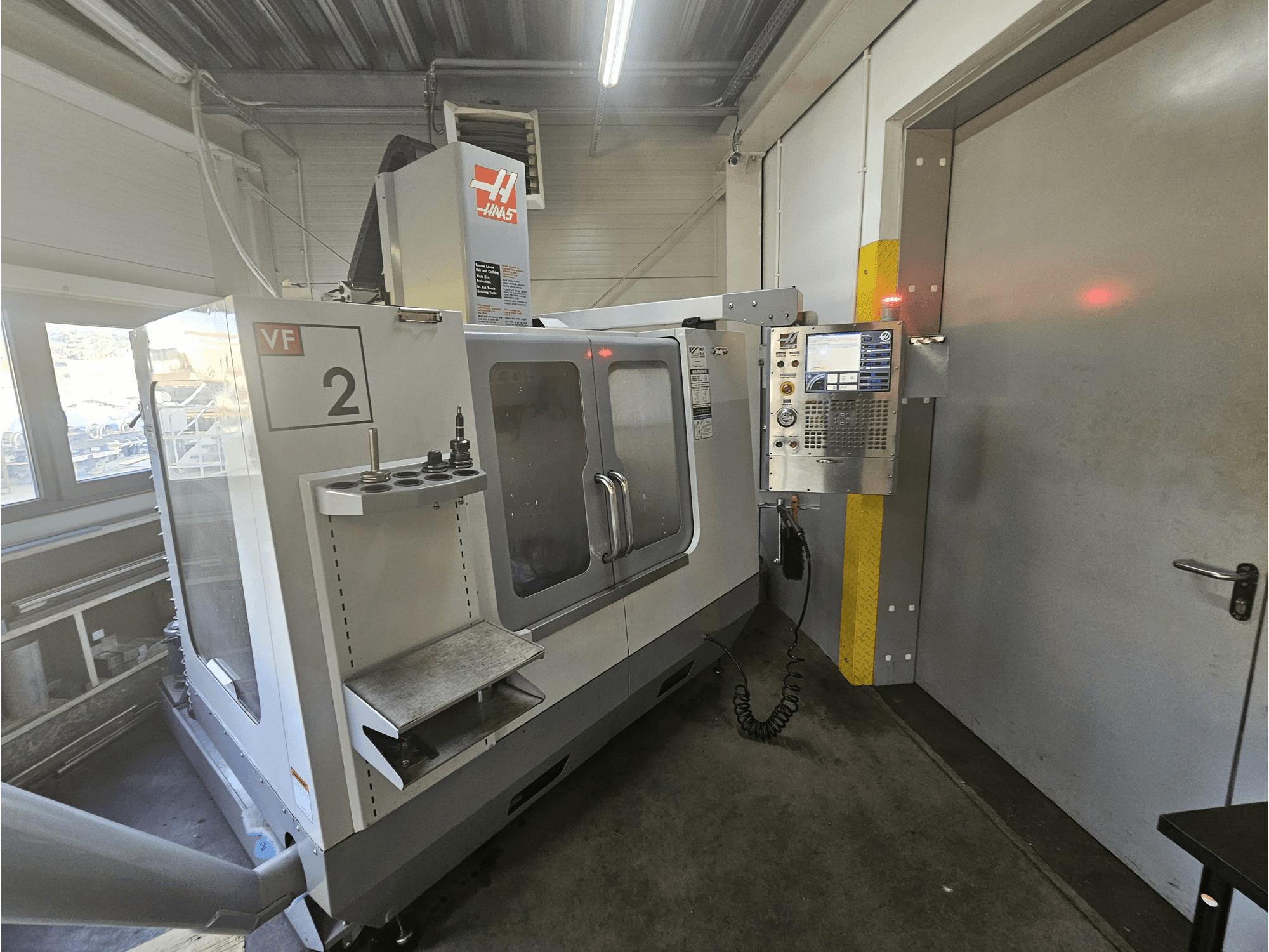Haas VF-2 CNC-Fräsmaschine, Vorderansicht, mit Bedienfeld, Werkzeughaltern und einem Sichtfenster auf den Arbeitsbereich.