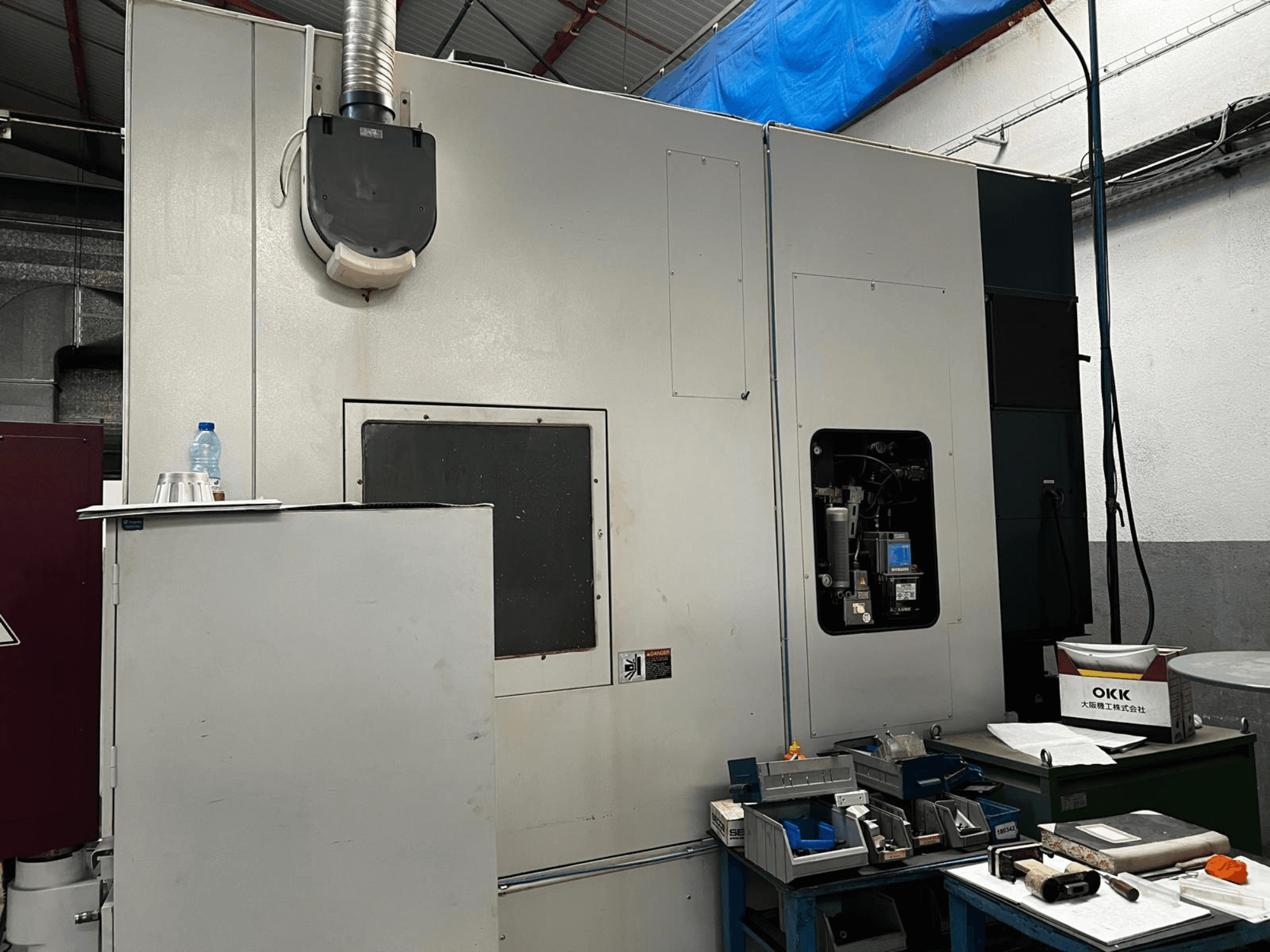 Vertikales Bearbeitungszentrum OKK VP600 in einer Werkstatt, Seitenansicht mit Details der Maschine und Werkzeugen auf einem Tisch in der Nähe.