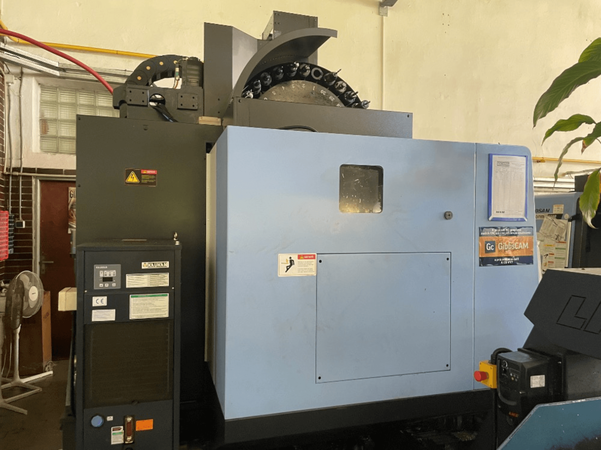 Vorderansicht eines vertikalen Bearbeitungszentrums DOOSAN DNM 5700 mit Bedienfeld, Sicherheitsschildern und Maschinenfunktionen.