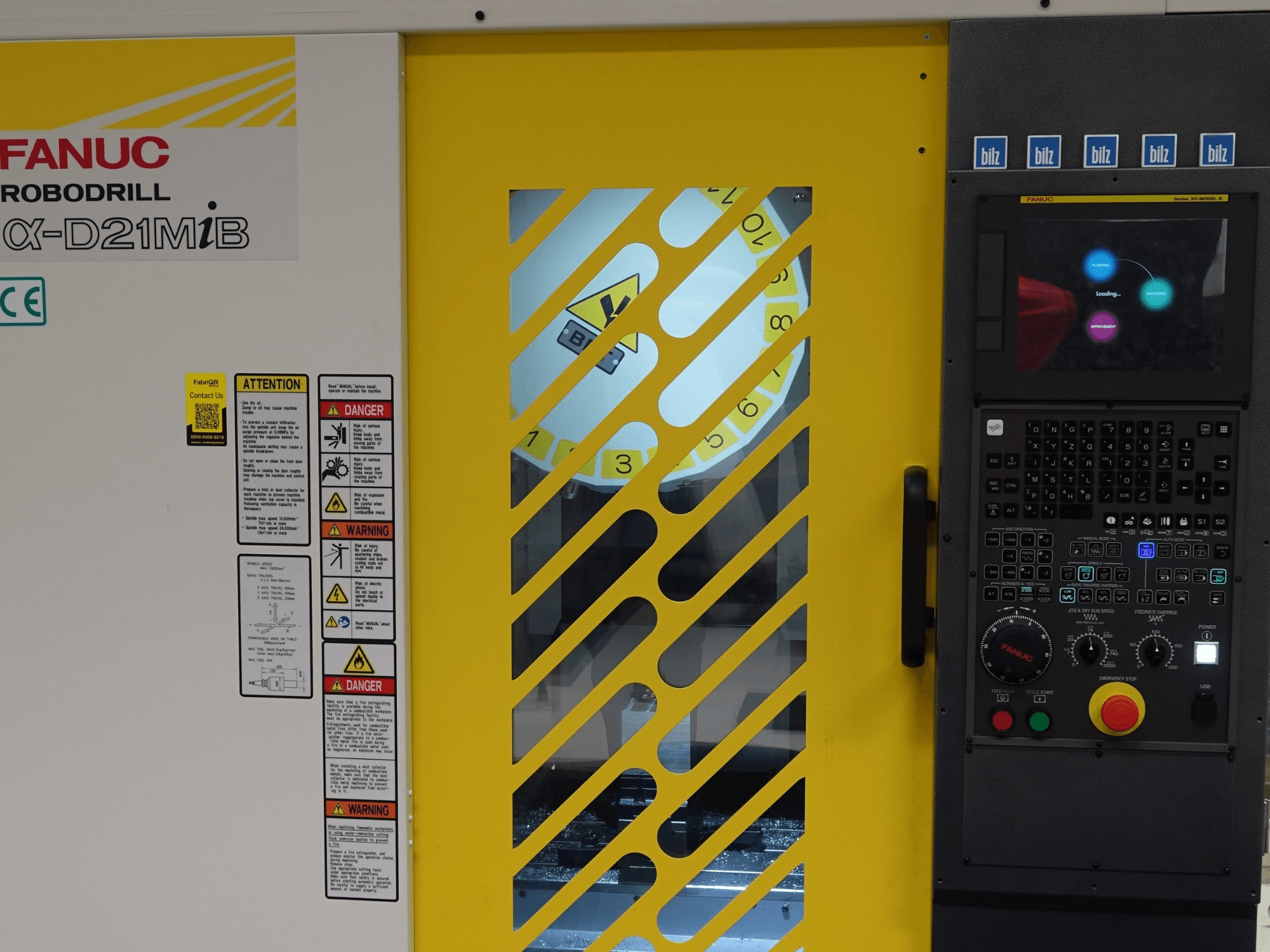 FANUC α-D21MiB Vertikales Bearbeitungszentrum in Frontansicht, mit Sicherheitshinweisen, Bedienfeld und gelber Sicherheitstür.