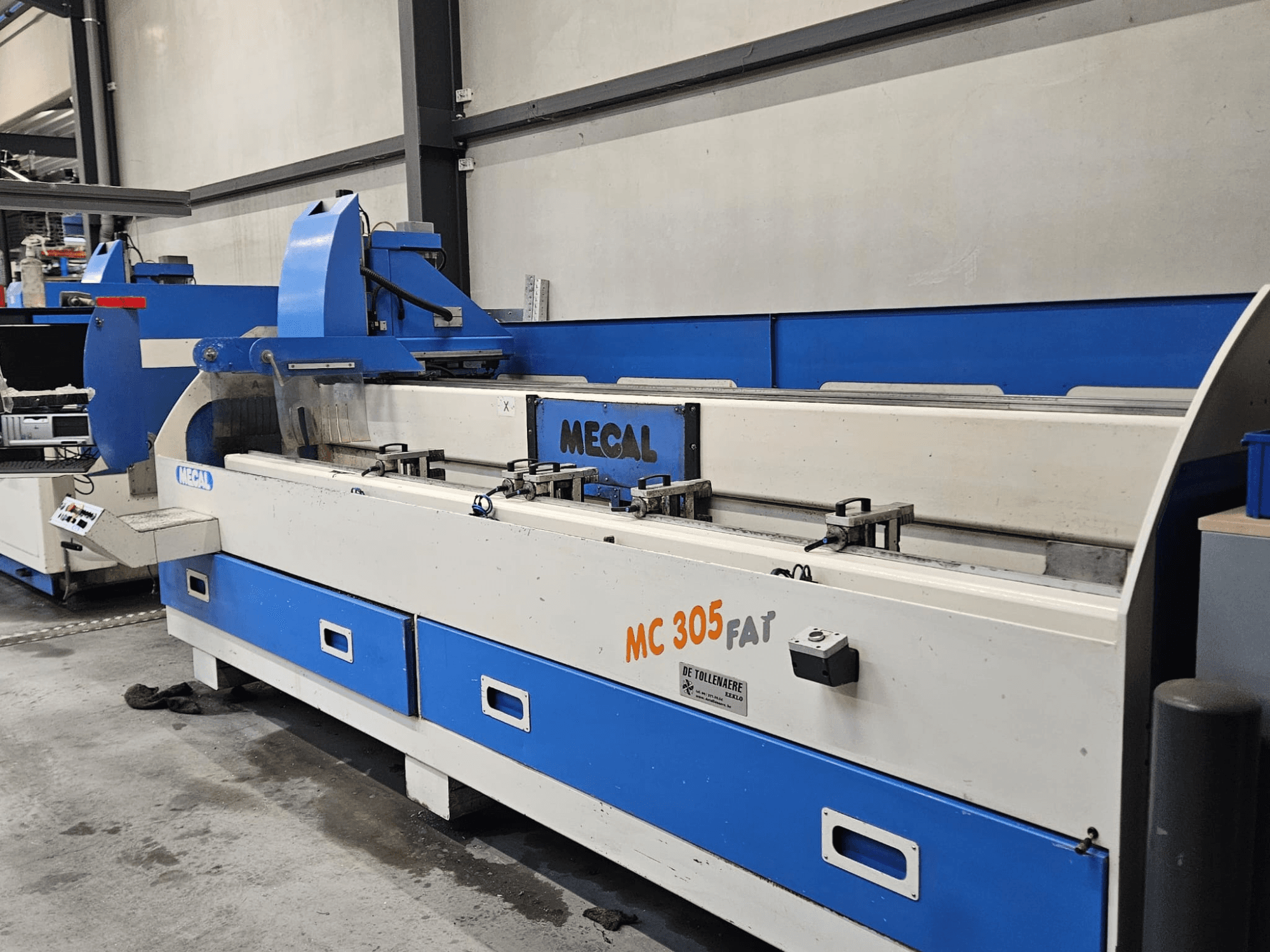 MECAL MC 305 FAT Maschine in einer Fabrikumgebung, Frontansicht mit Bedienelementen und blau-weißem Design.