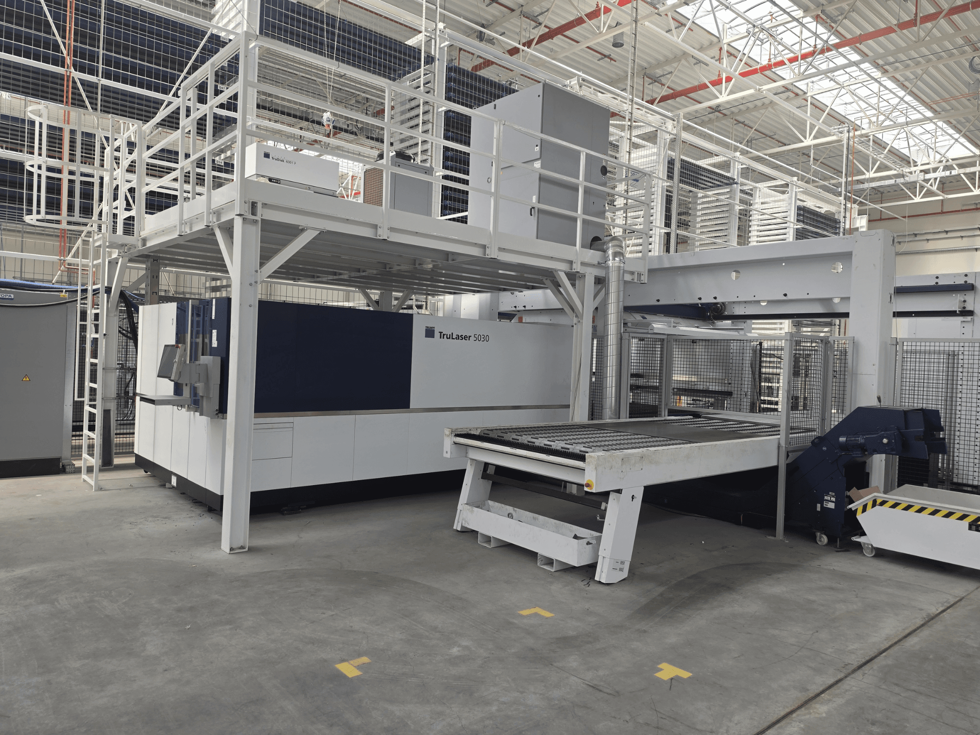 TRUMPF TruLaser 5030 fiber L76 FMC-Maschine in einer Werkstatt, Vorderansicht mit Schneidbereich und Be- und Entladevorrichtung.