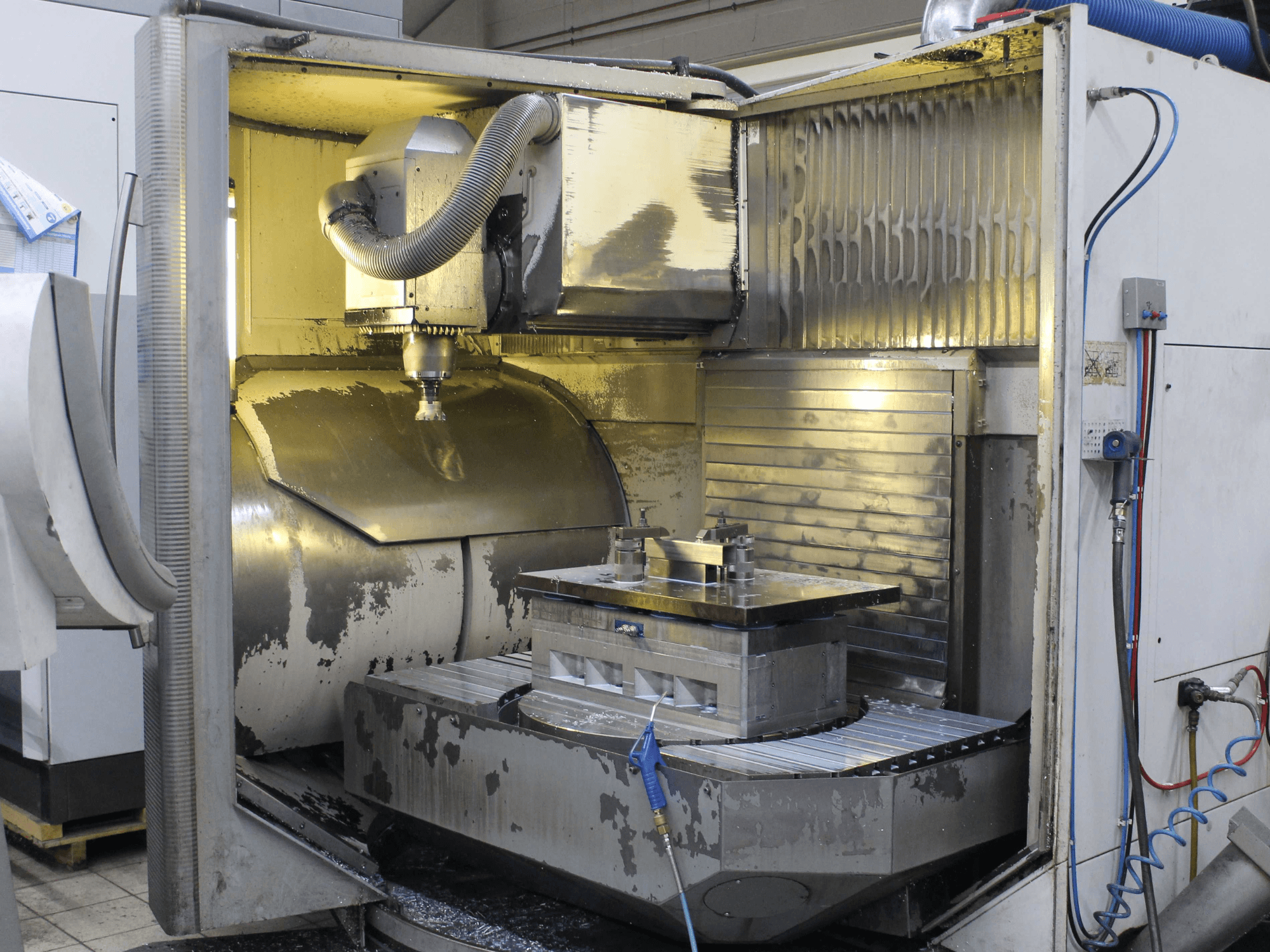 CNC-Fräsmaschine innen, Seitenansicht, zeigt Werkstück und Schneidwerkzeug mit Metallspänen und Kühlmittelrückständen.