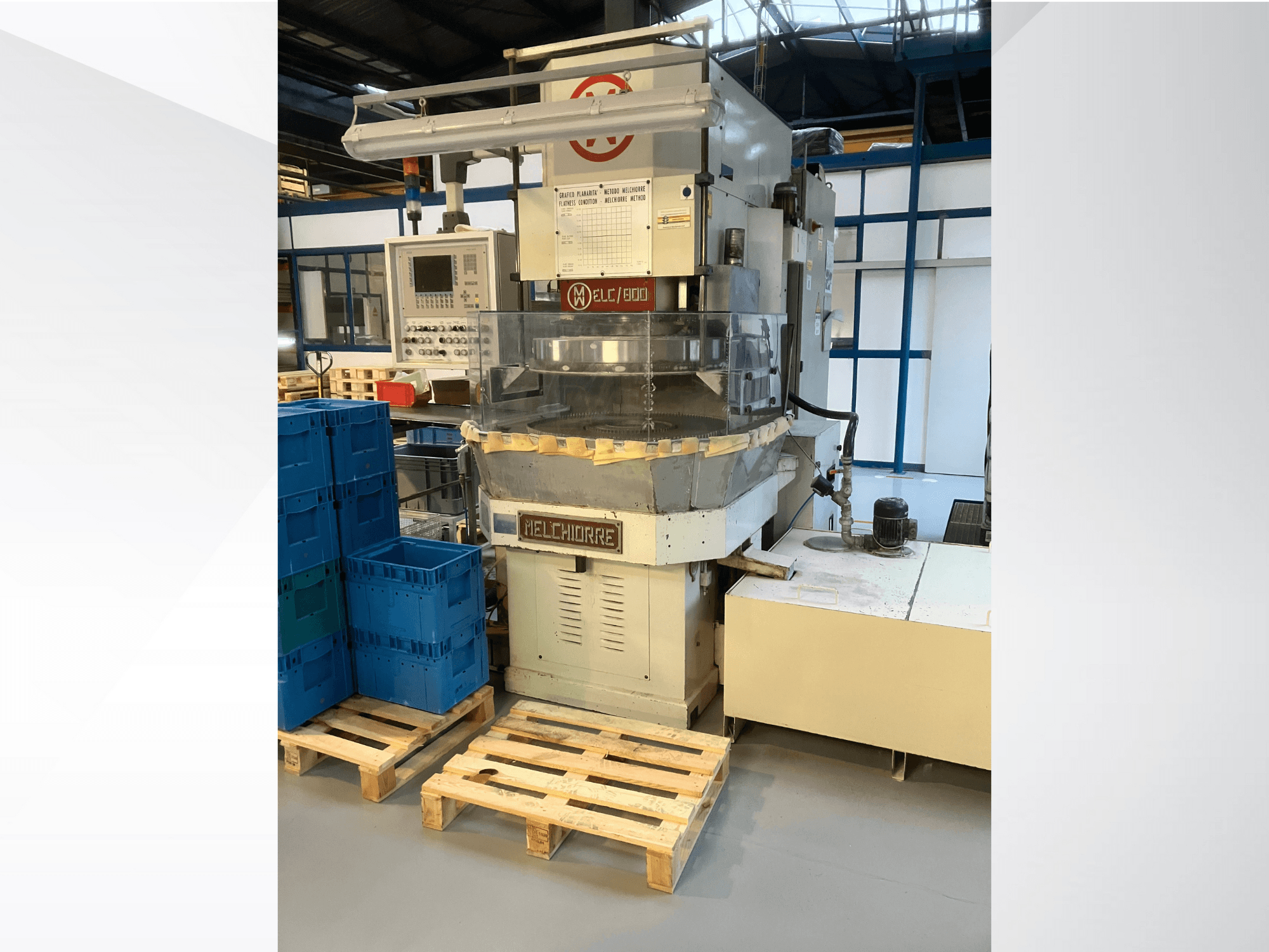 Melchiorre-Industriemaschine in der Vorderansicht, mit Bedienfeld, durchsichtigem Trichter und blauen Kisten auf Holzpaletten.
