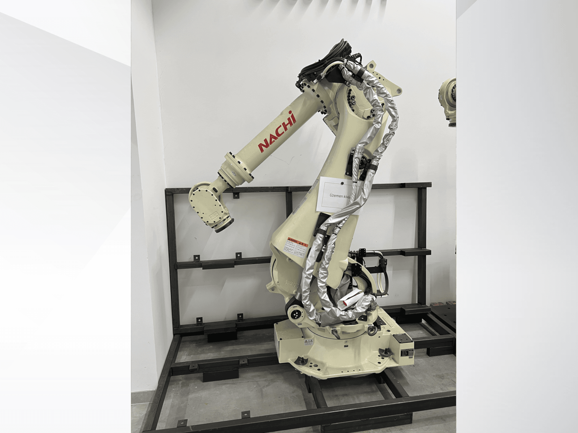 Roboterarm NACHI SRA166-01 in der Seitenansicht, mit flexiblen Gelenken, befestigten Kabeln und montiert auf einem Schutzrahmen.