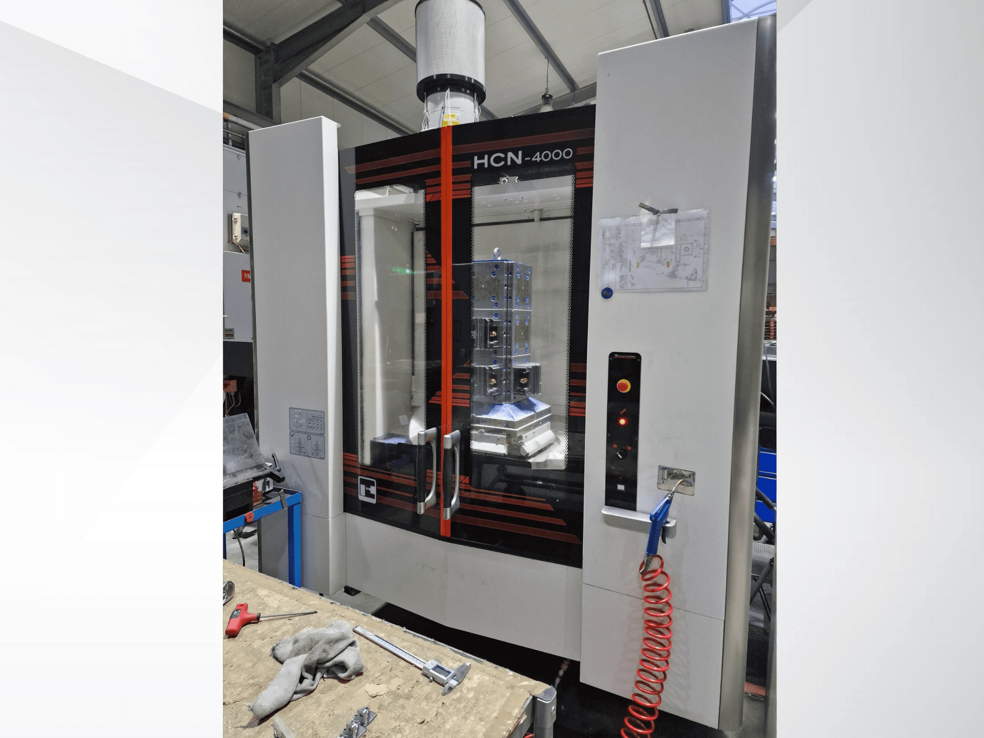 HCN-4000 CNC-Maschine in der Vorderansicht, mit Glasscheibe, Bedienfeld mit Tasten und angehängtem Bauplan.