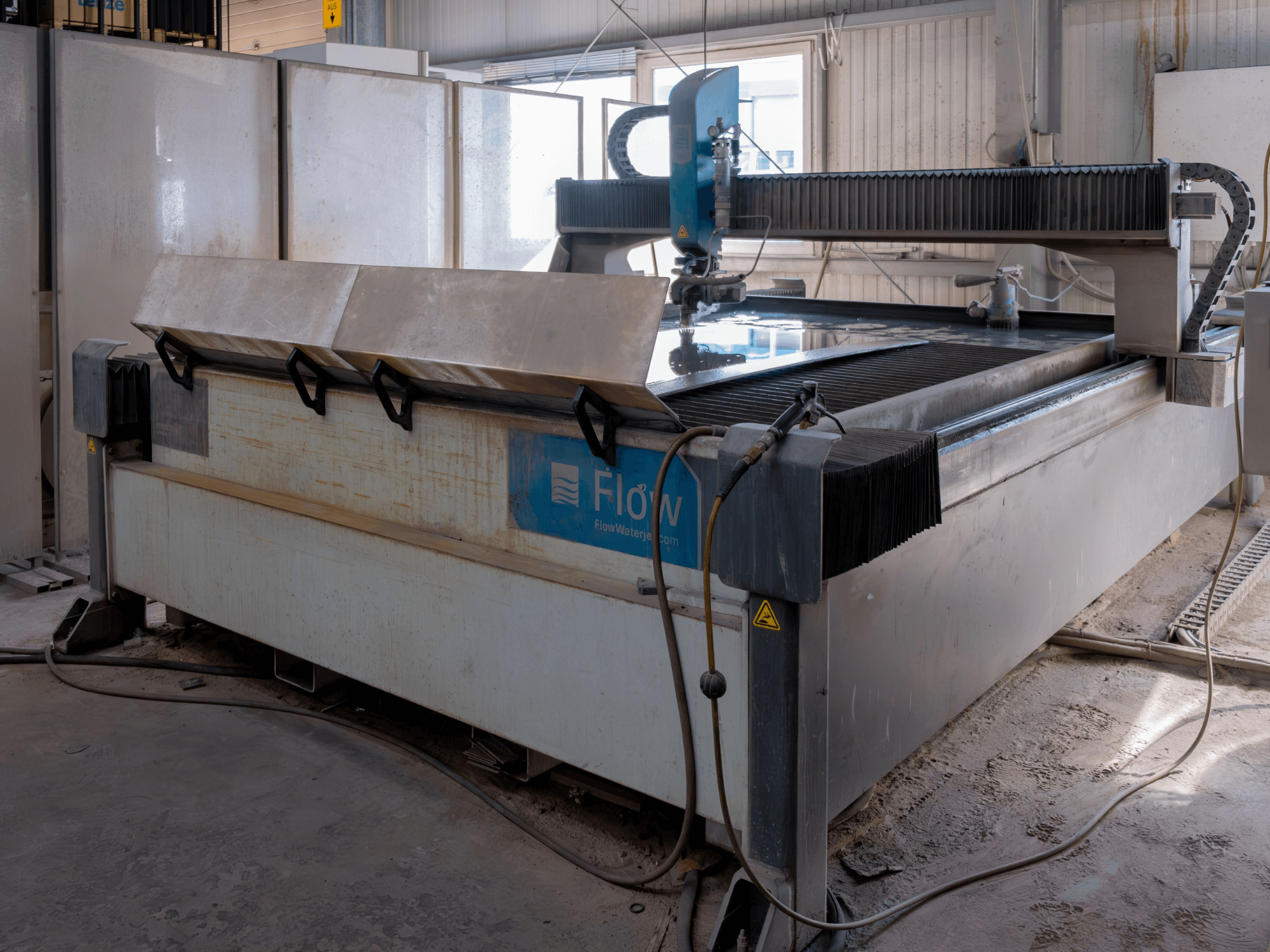 Flow KENT Mach 2 C Wasserstrahlschneidanlage in einer Seitenansicht, die den Schneidtisch aus Edelstahl und die Wasserstrahldüse zeigt.