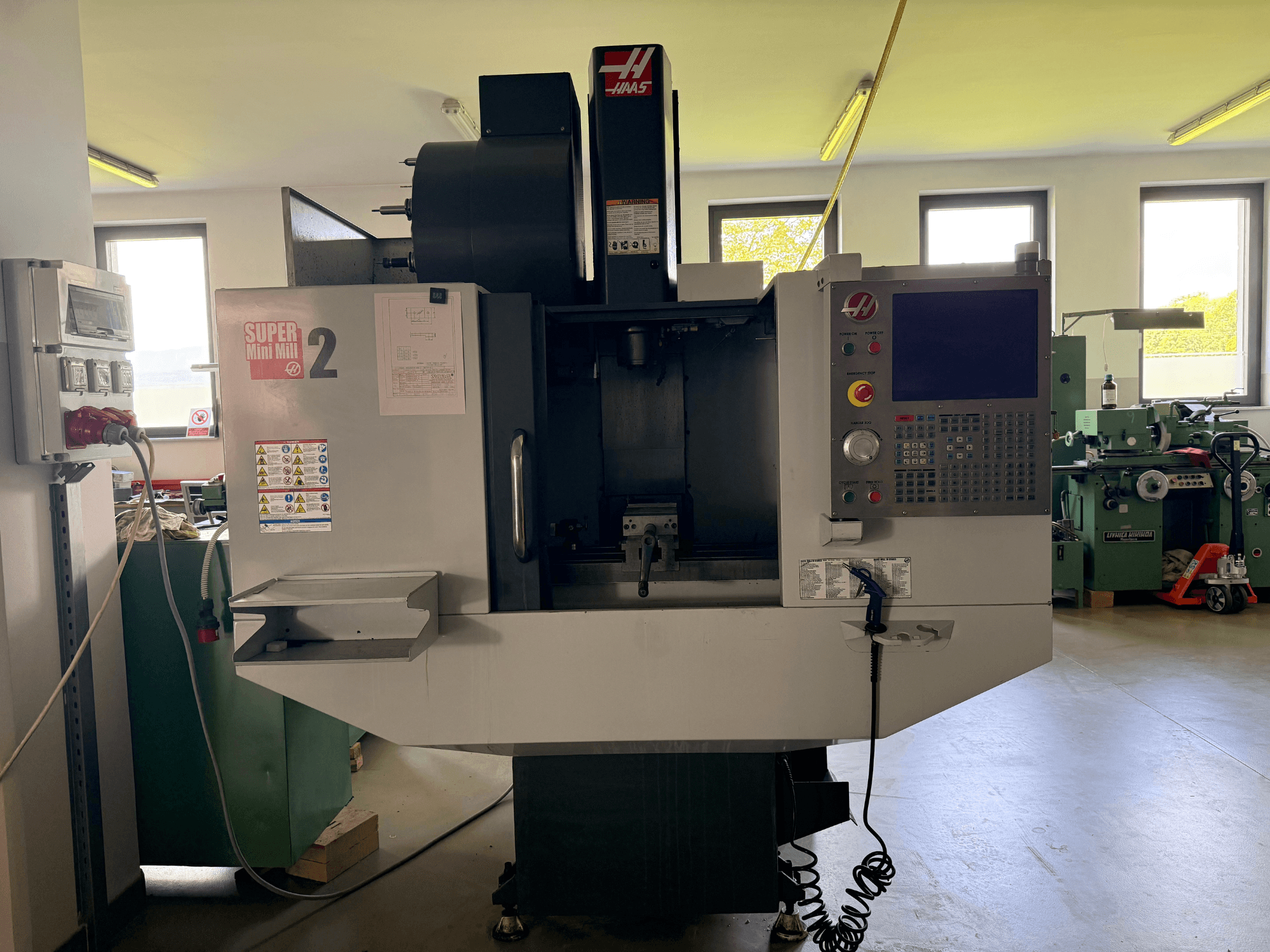 Haas Mini Mill 2 Vertikal-Bearbeitungszentrum in der Vorderansicht, mit Bedienfeld und Werkzeugbereich mit Warnhinweisen.