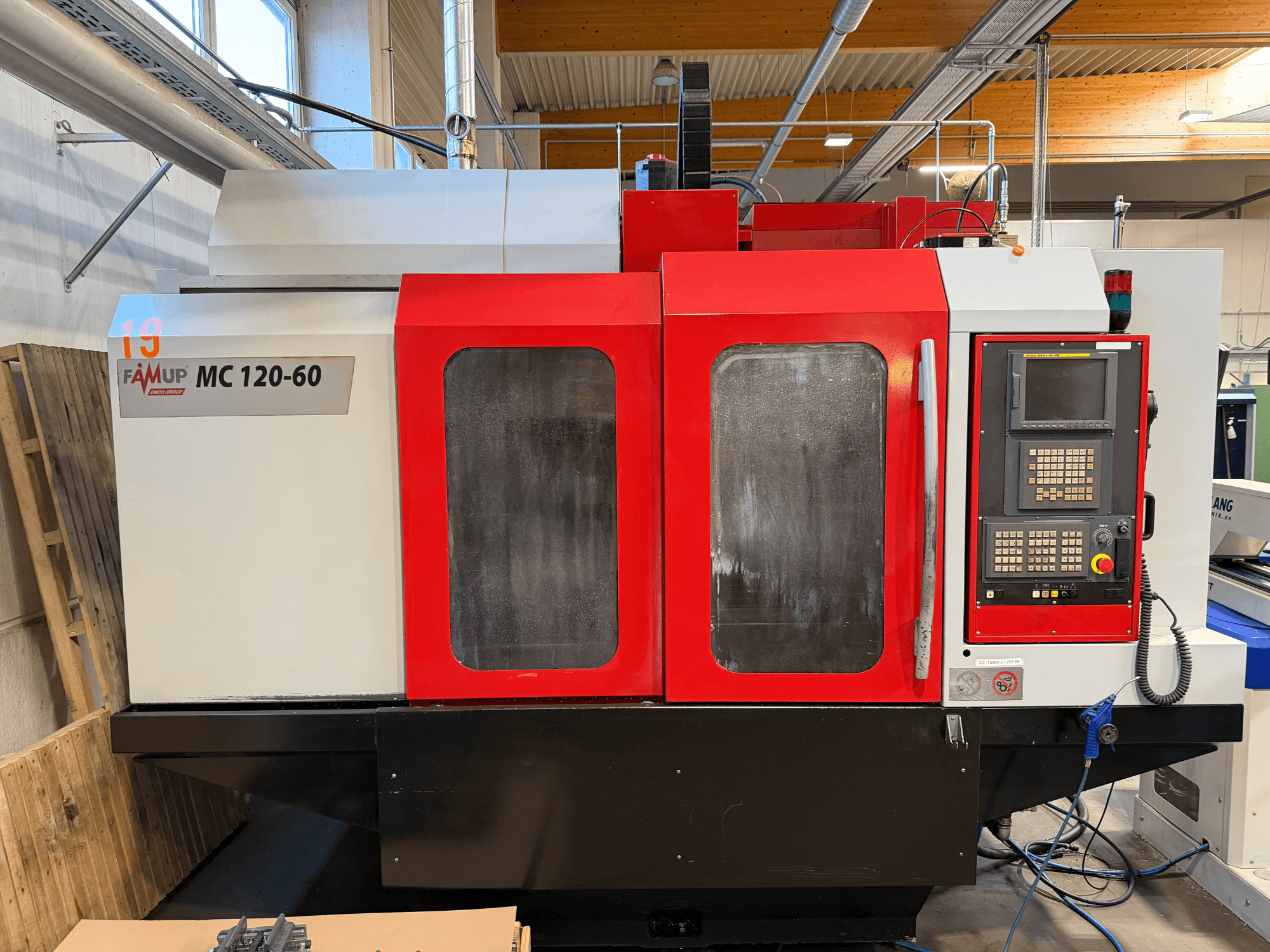 Frontansicht des vertikalen Bearbeitungszentrums EMCO MC 120-60 mit rot-weißem Gehäuse, Bedienfeld und Bildschirm.