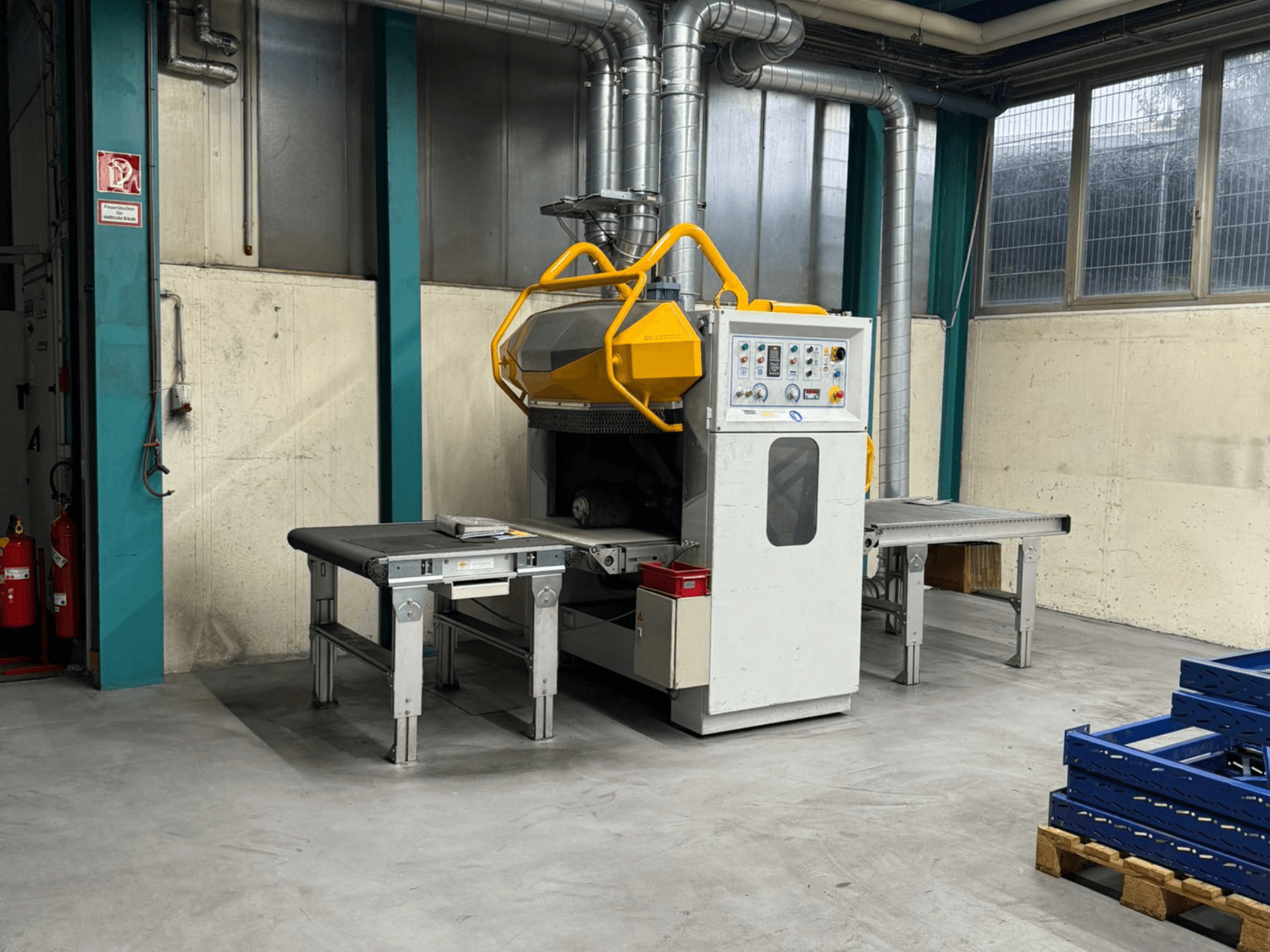 Entgratungsmaschine Fladder AUT-1000 VAC in einer Fabrikumgebung, mit Bedienfeld, gelber Schutzvorrichtung und angrenzenden Arbeitstischen.