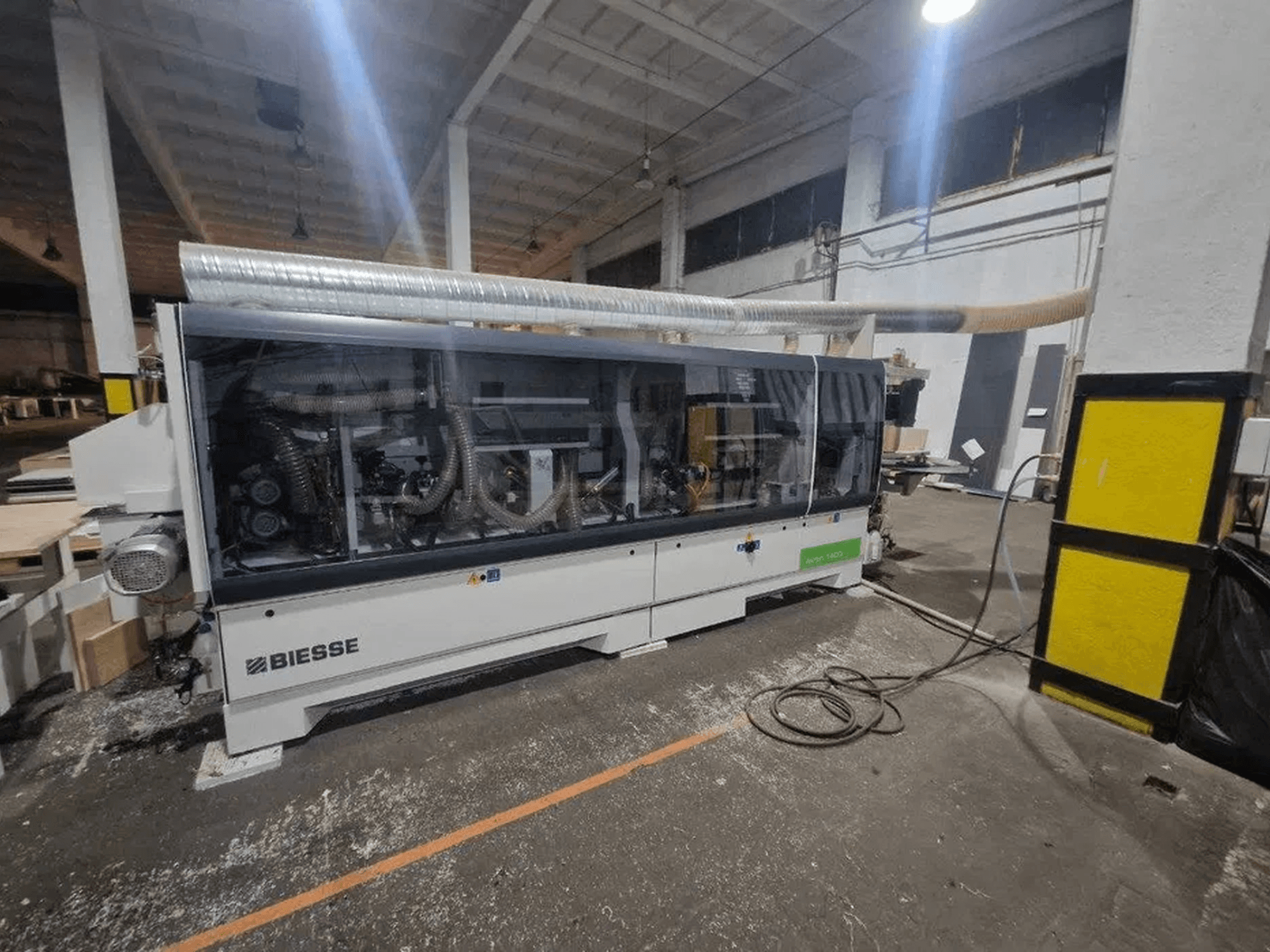 Eine BIESSE Akron 1440 A Kantenanleimmaschine in einer Werkstatt, mit transparenter Abdeckung und sichtbaren Maschinenkomponenten.