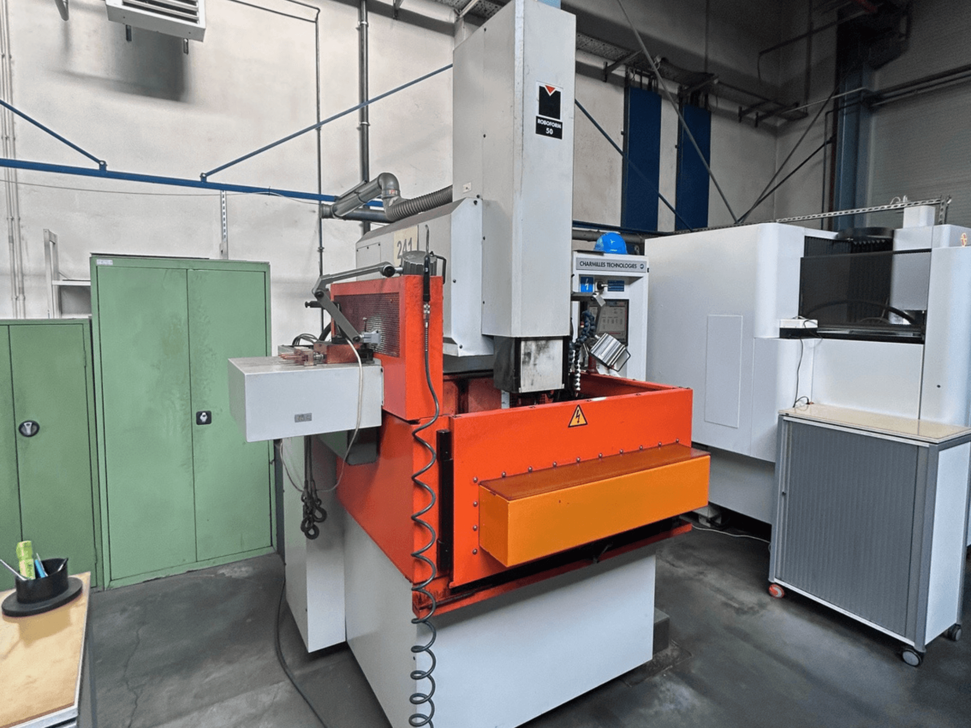 Frontansicht der CHARMILLES ROBOFORM 50 Senkerodiermaschine mit orangefarbenem Bedienfeld, Steuerungsschnittstelle und umliegenden Geräten.
