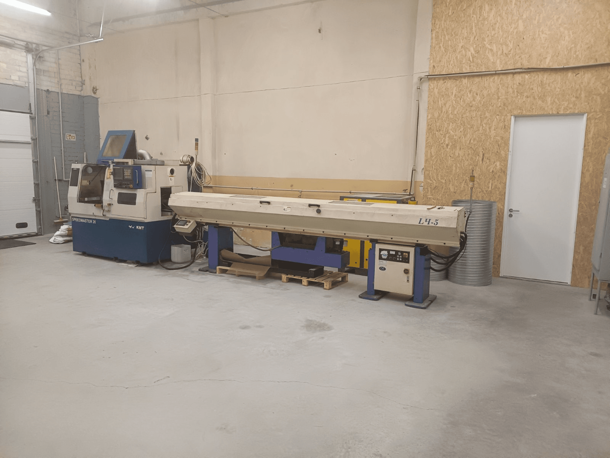 Industriehalle mit KMT Speedmaster 34 und L4.5, von vorne gesehen, mit sichtbaren Bedienelementen und Maschinen.