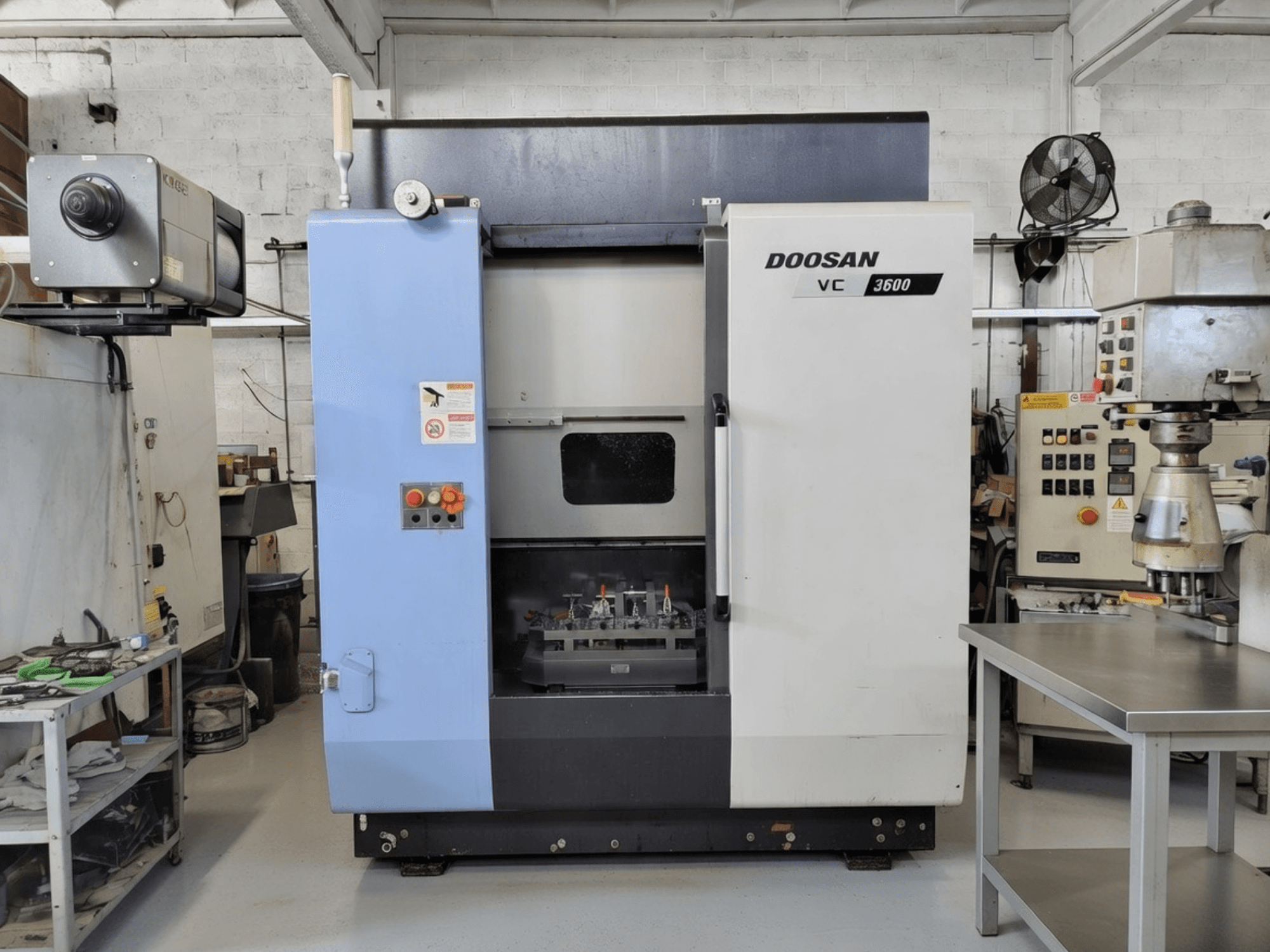 Vertikales Bearbeitungszentrum DOOSAN VC 3600 in der Vorderansicht mit Bedienfeld und offener Tür zum Arbeitsraum.