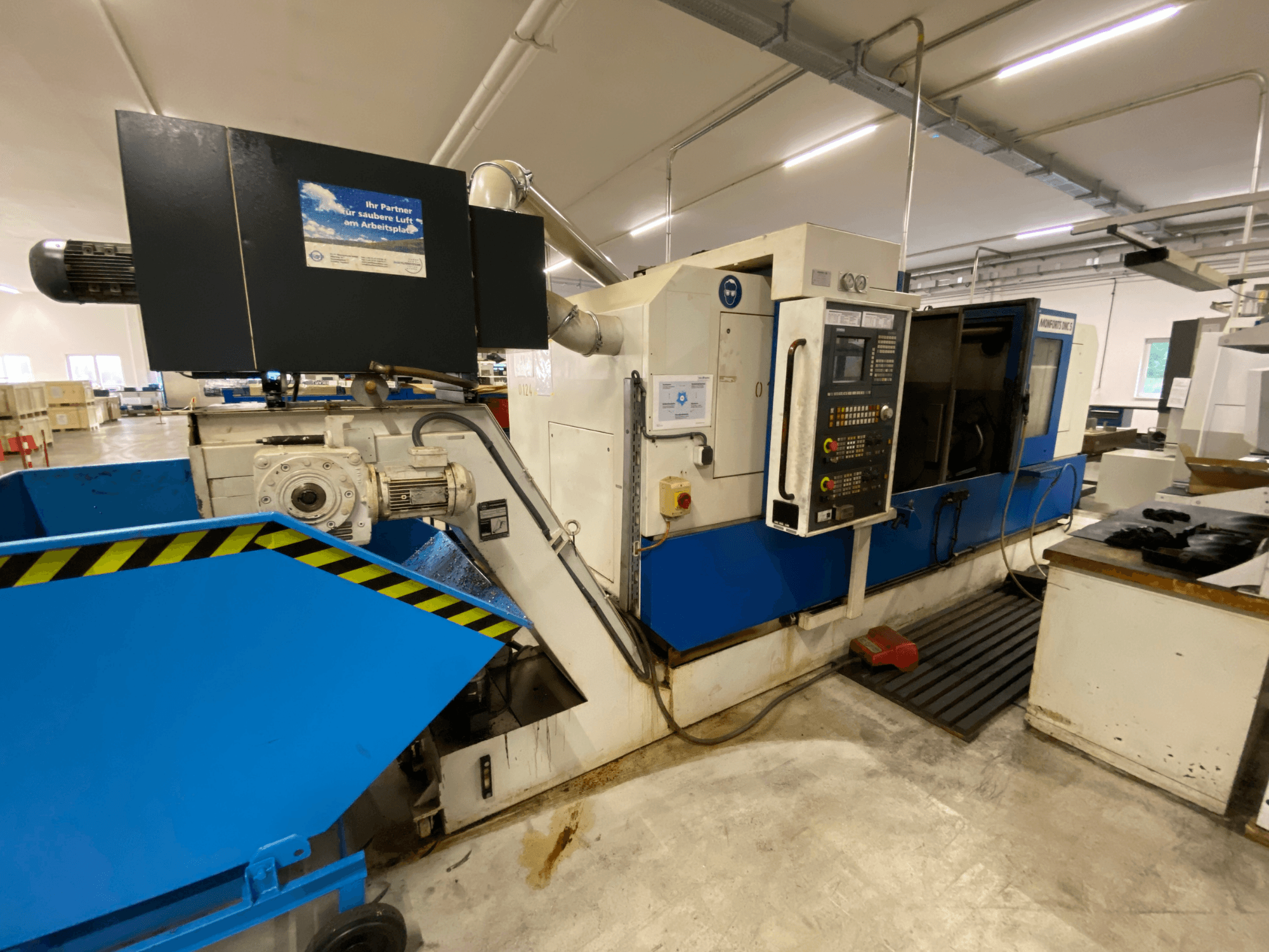 Monforts DNC 5 Dreh-Fräszentrum, Seitenansicht mit Bedienfeld, blauer Späneauffangschale und Maschinendetails in einer Werkstattumgebung.