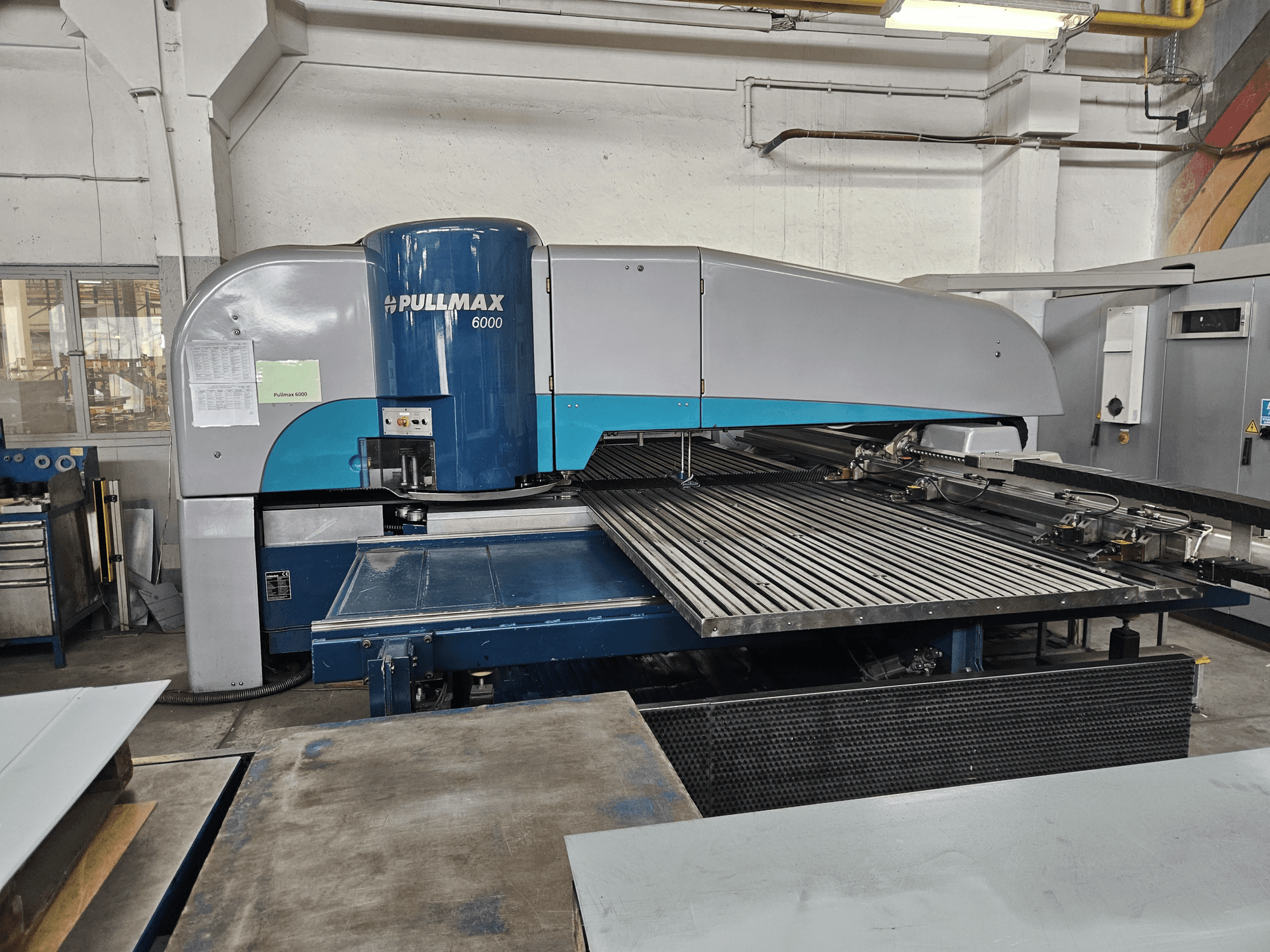 Frontansicht der Pullmax 6000 CNC-Stanzmaschine, die ihr großes Flachbett und den Metallrahmen in einer Werkstattumgebung zeigt.