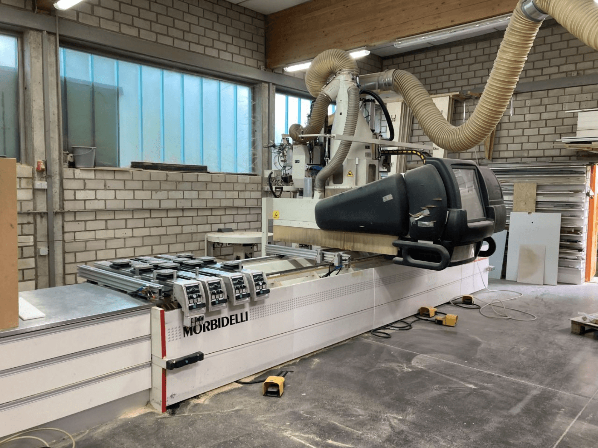 MORBIDELLI CNC-Maschine in einer Werkstatt, Vorderansicht mit Bedienfeld, Absauganlage und positioniertem Holzstück.