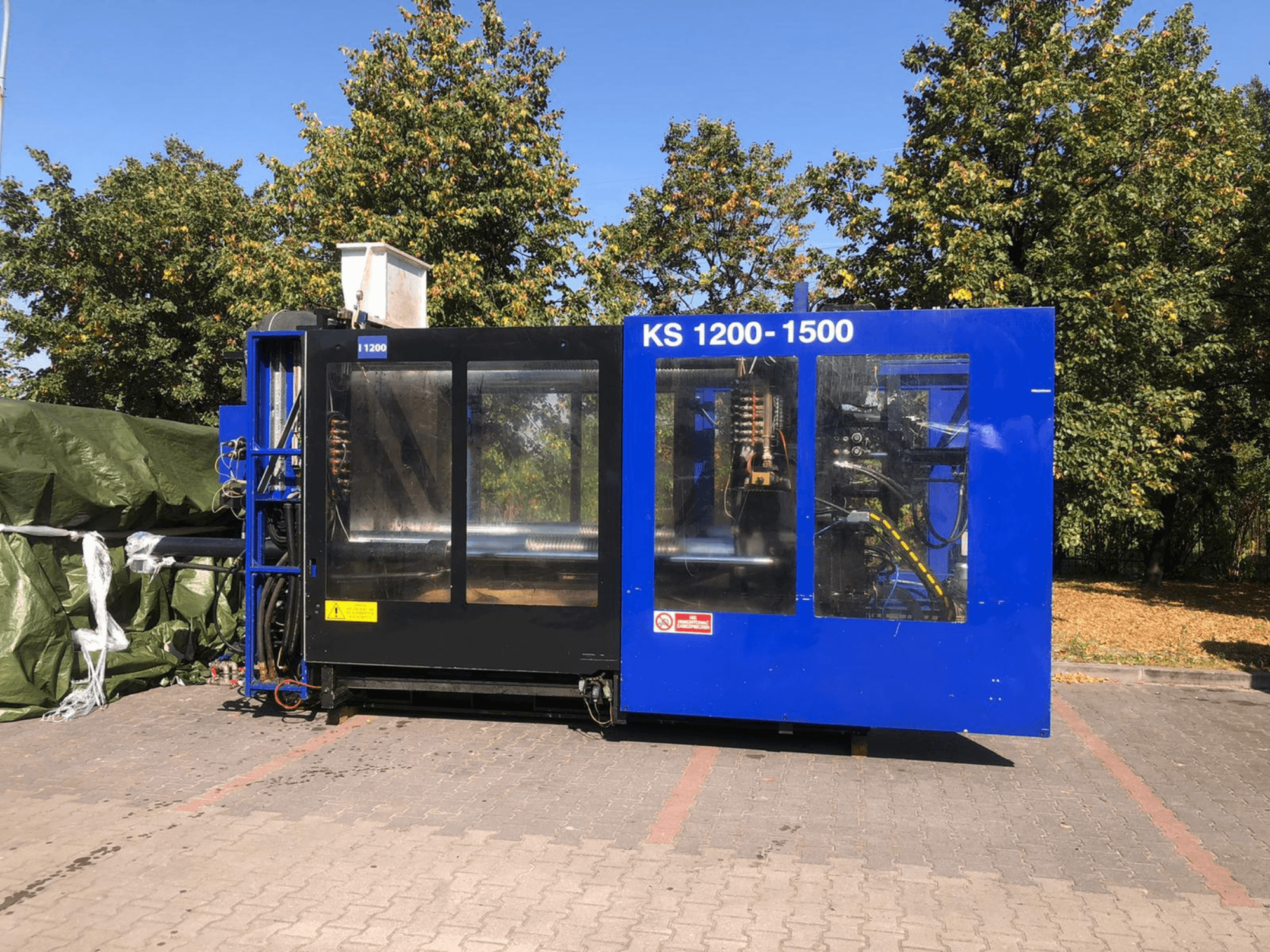 Hydraulische Spritzgießmaschine ITALTECH KS 1200 8300 ES, Seitenansicht, zeigt die Bedienelemente und Maschinendetails in einer Parklandschaft.