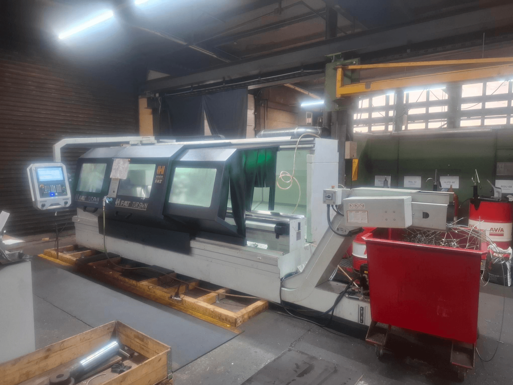 Vorderansicht einer FAT Tursan CNC-Maschine mit Bedienfeld, die auf Holzpaletten in einer Werkstatt steht.