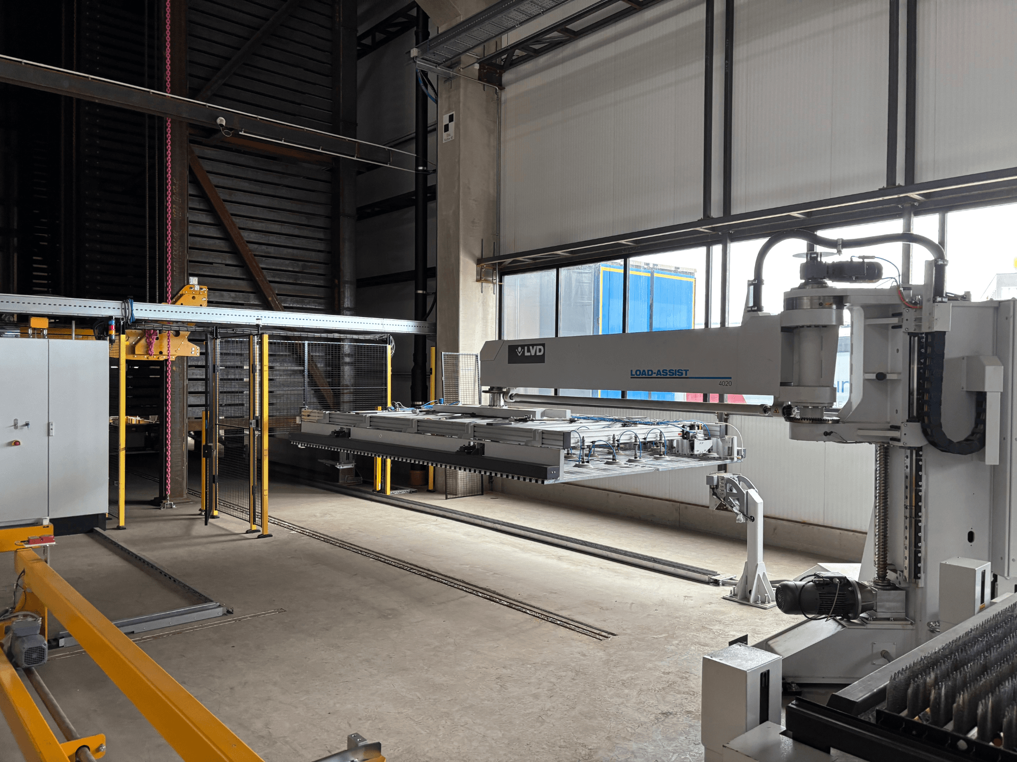 LVD Load-Assist 4020 Automatisierungsausrüstung in einer Frontansicht mit einem Roboterarm und einem Ladesystem, das in einem großen Arbeitsbereich sichtbar ist.
