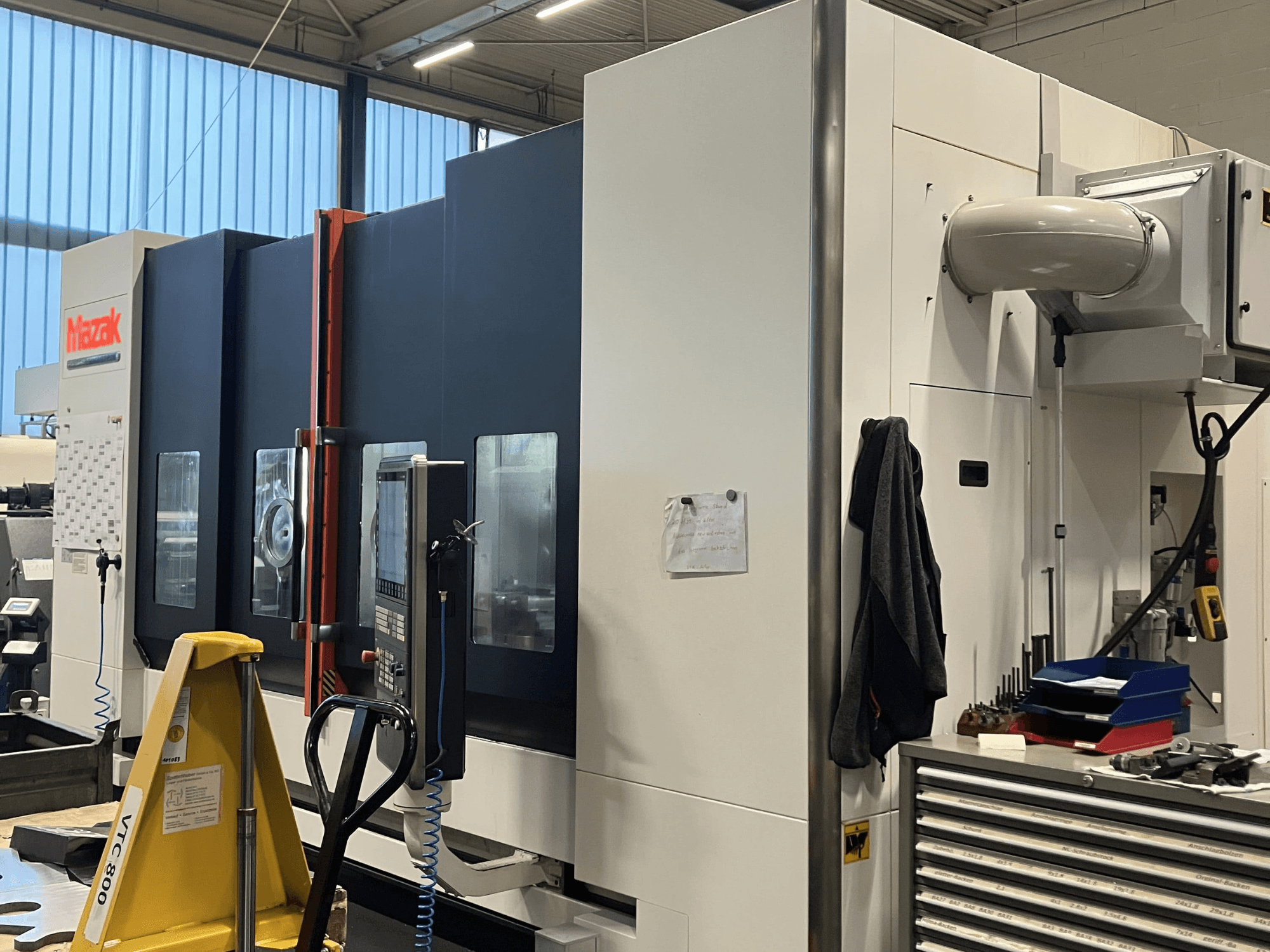 Mazak CNC-Maschine in der Seitenansicht, die das Bedienfeld und die Sicherheitsfunktionen in einer Werkstattumgebung zeigt.